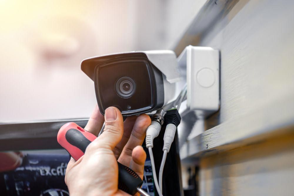 A Person Is Fixing A Security Camera With A Screwdriver — On Guard Security & Communications In Wallsend, NSW