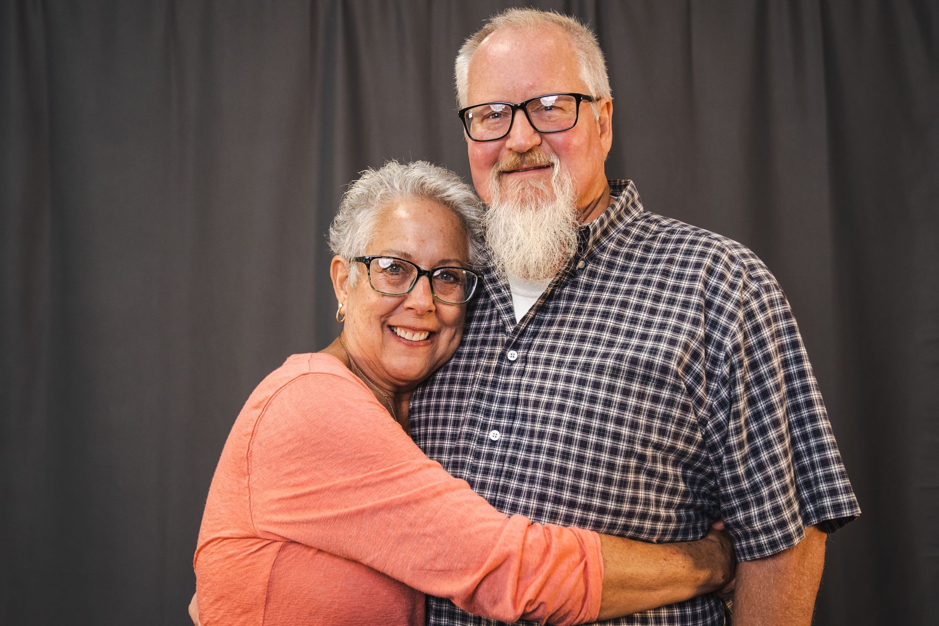 A man and a woman are hugging each other in front of a black curtain.