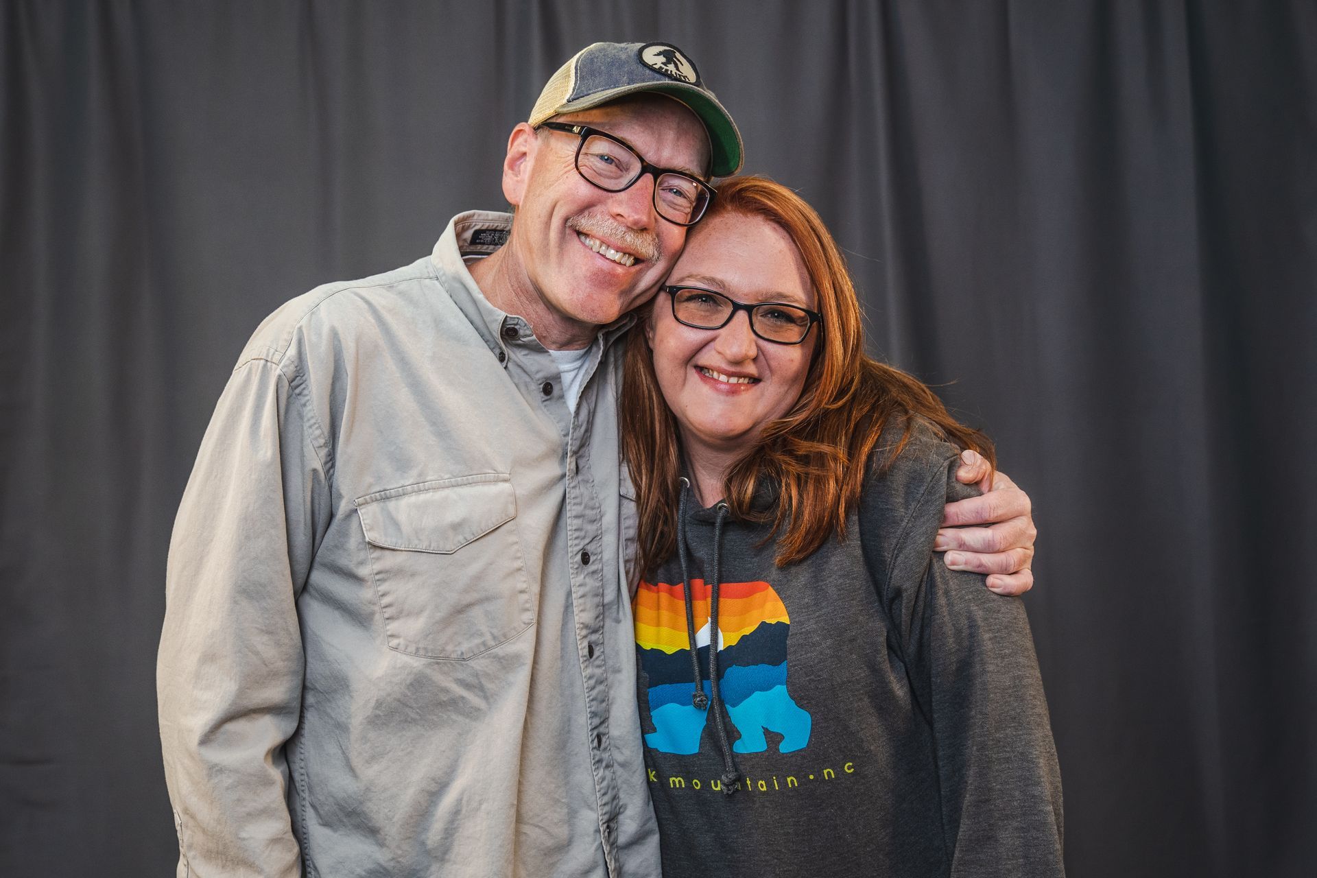 A man and a woman are posing for a picture in front of a black curtain.