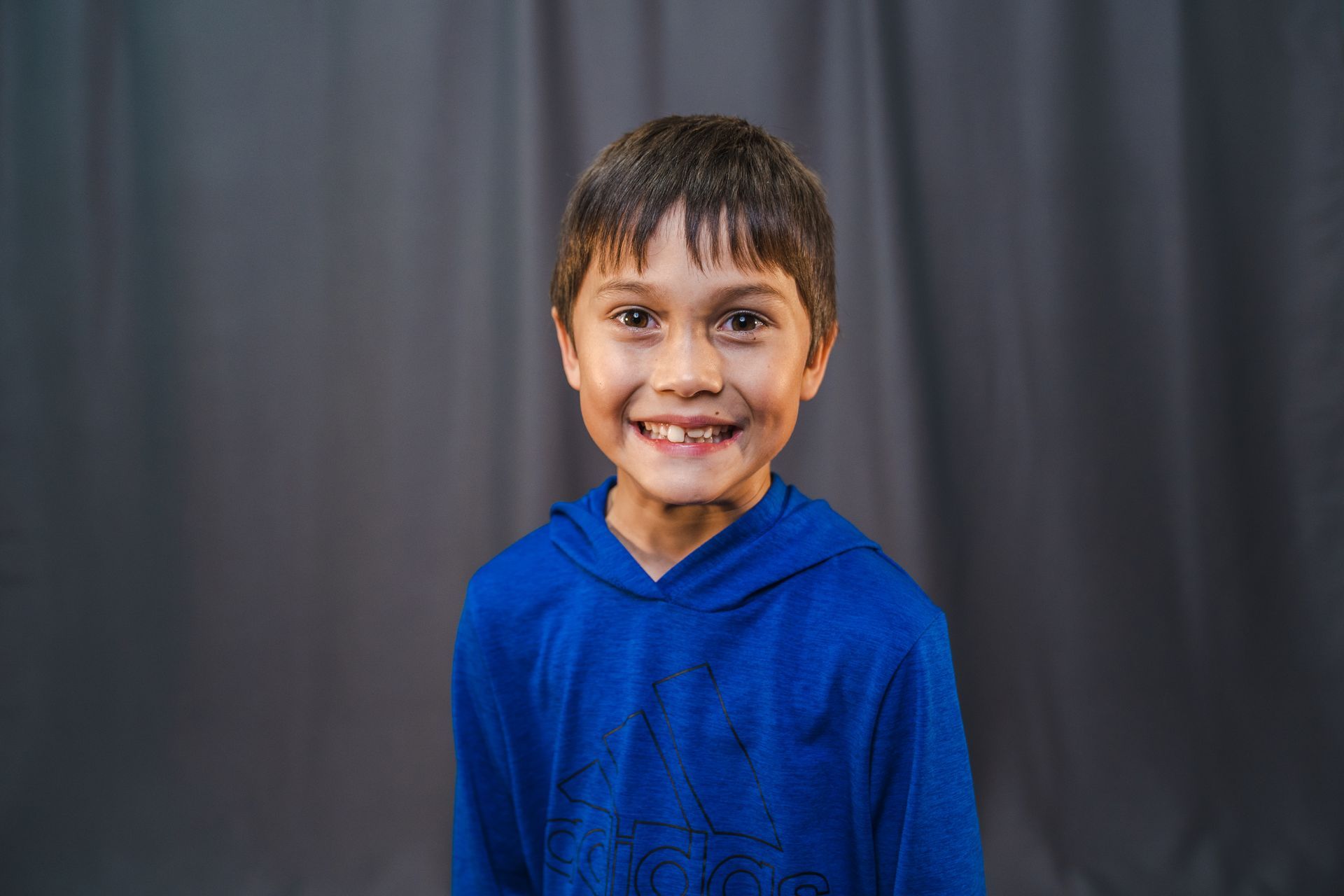 A young boy in a blue hoodie is smiling for the camera.