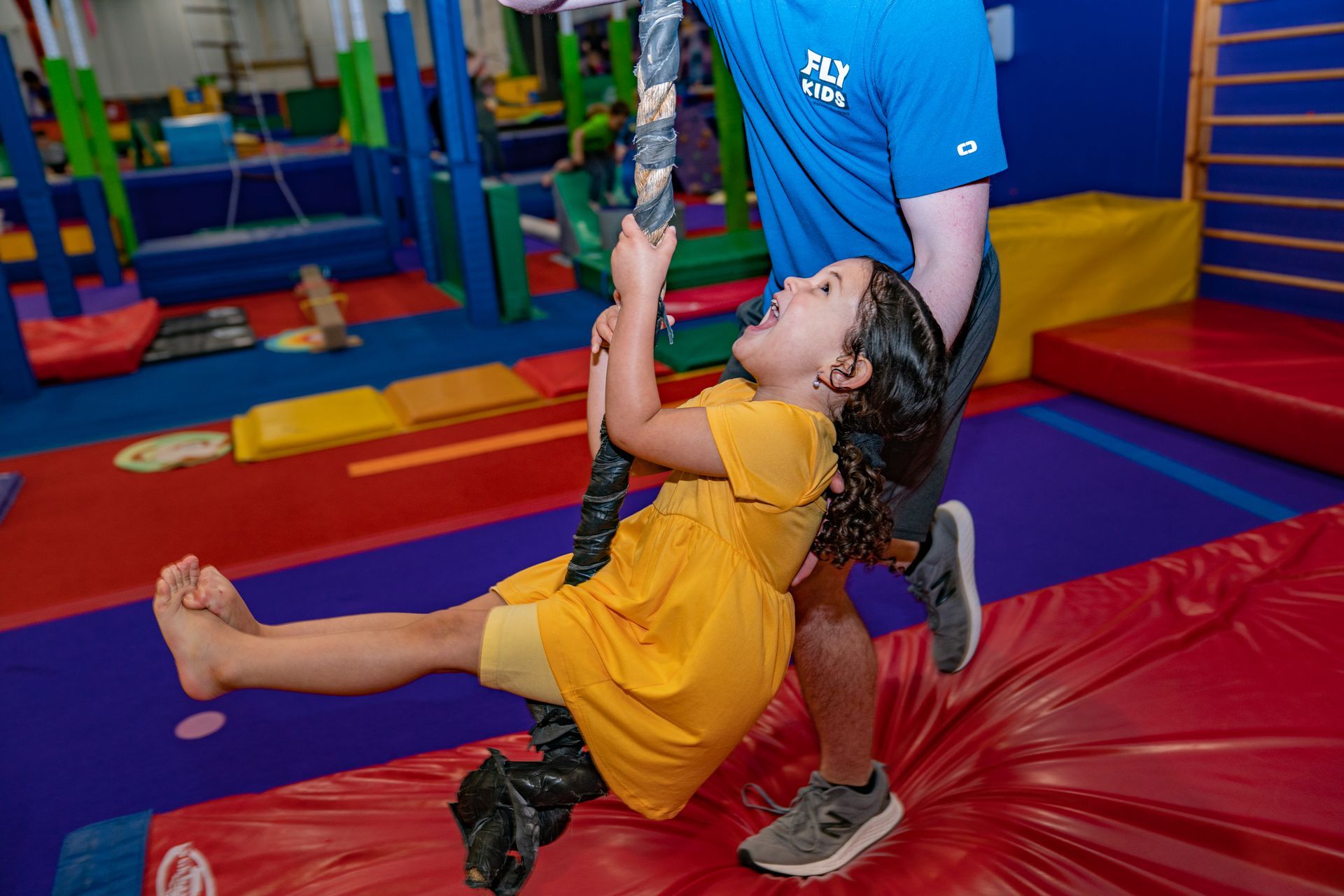 A man is carrying a little girl on a rope in a gym.