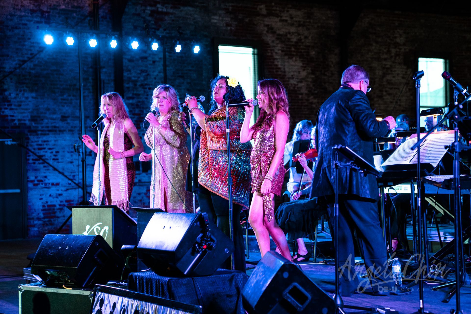 A group of women singing on a stage with a man playing a keyboard