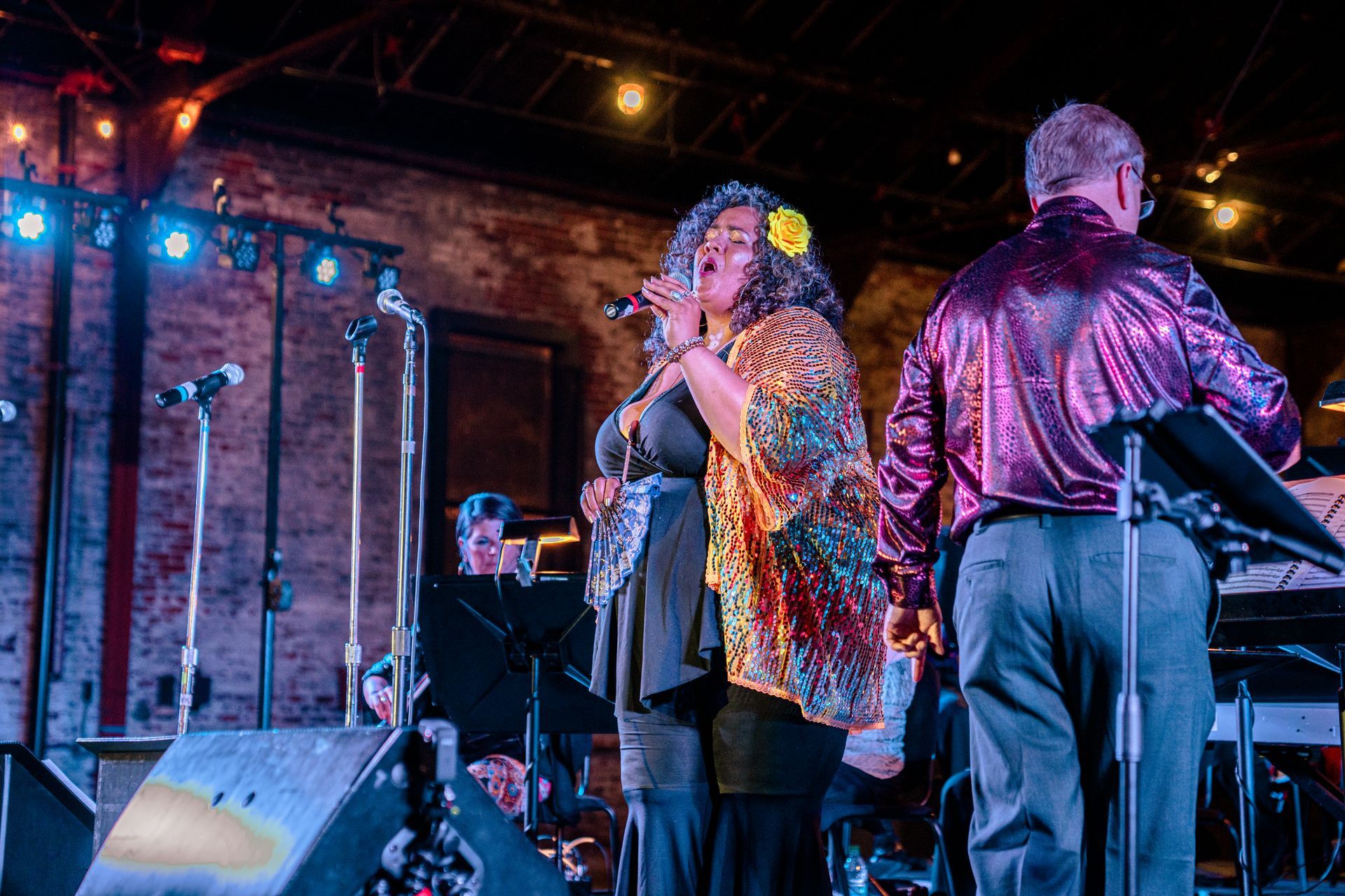 A woman is singing into a microphone on stage while a man plays a keyboard.
