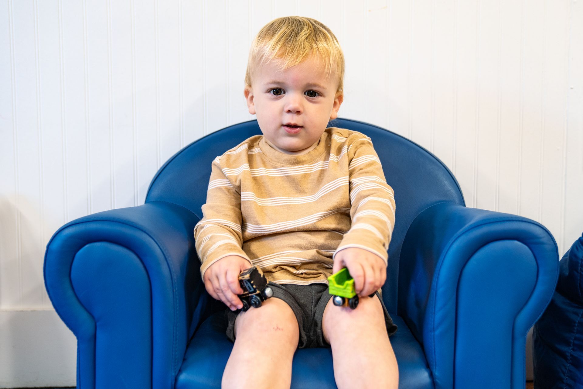 A young boy is sitting in a blue chair holding a toy train.