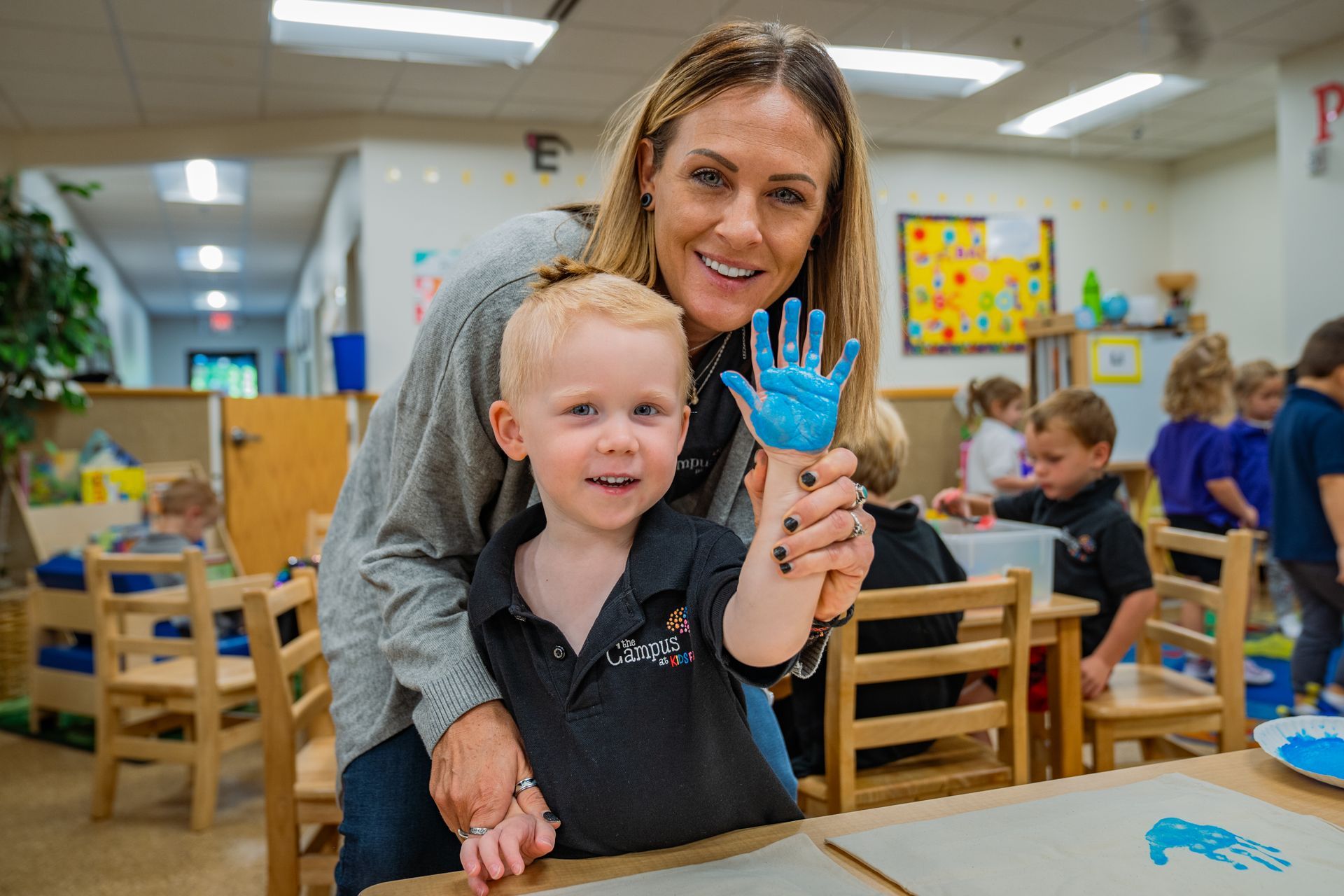 A woman is holding a child 's hand painted blue in a classroom.