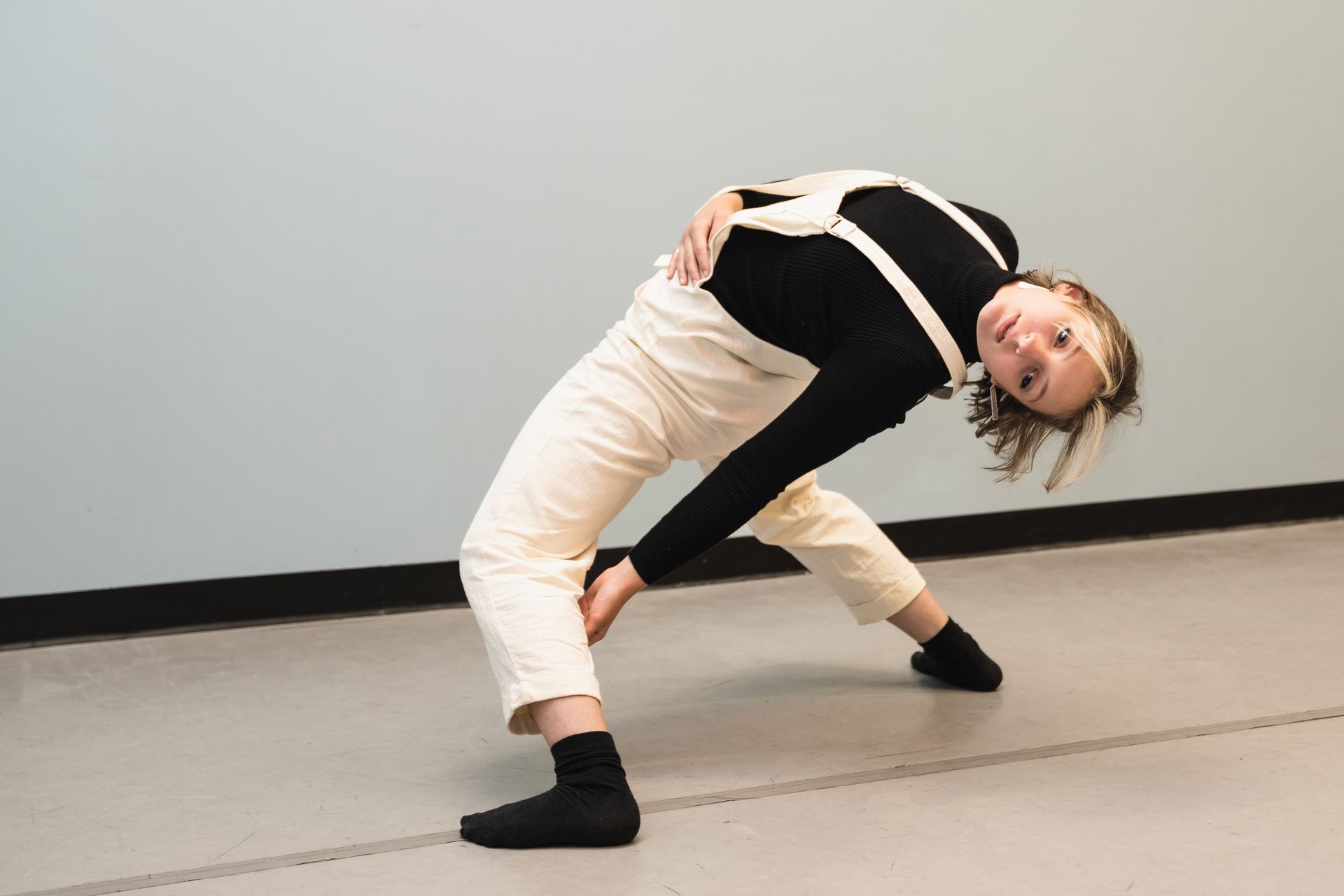 A woman in white overalls and black socks is dancing on a dance floor.
