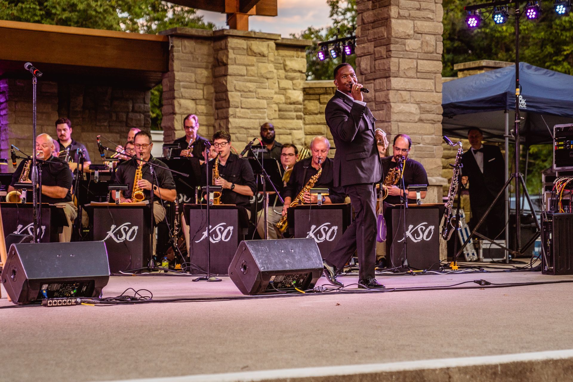 A man is singing into a microphone in front of an orchestra on a stage.