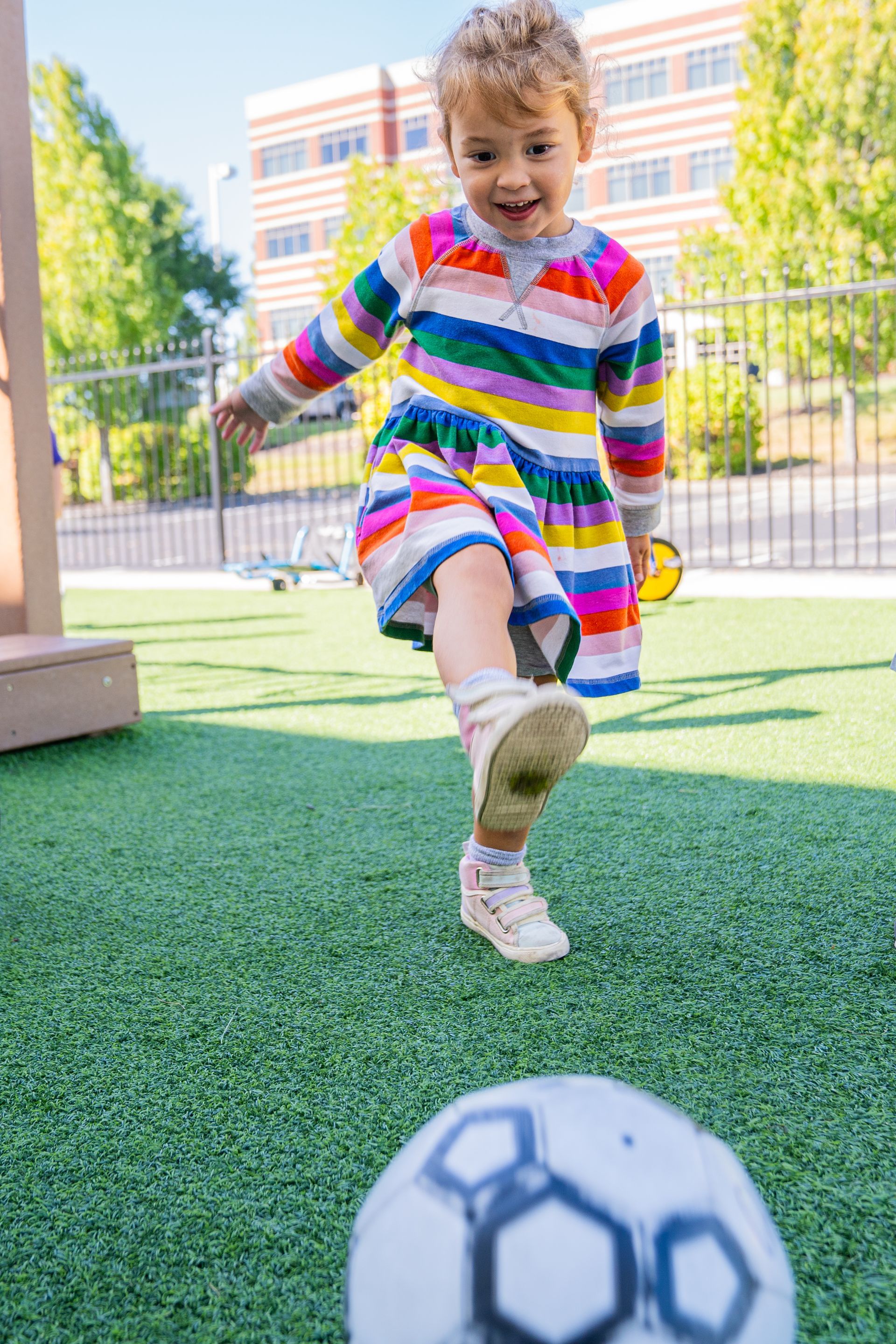 A little girl is kicking a soccer ball on a field.