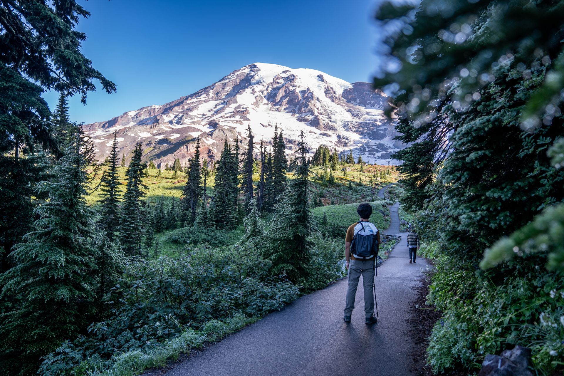 A man with a backpack is standing on a path in front of a mountain.
