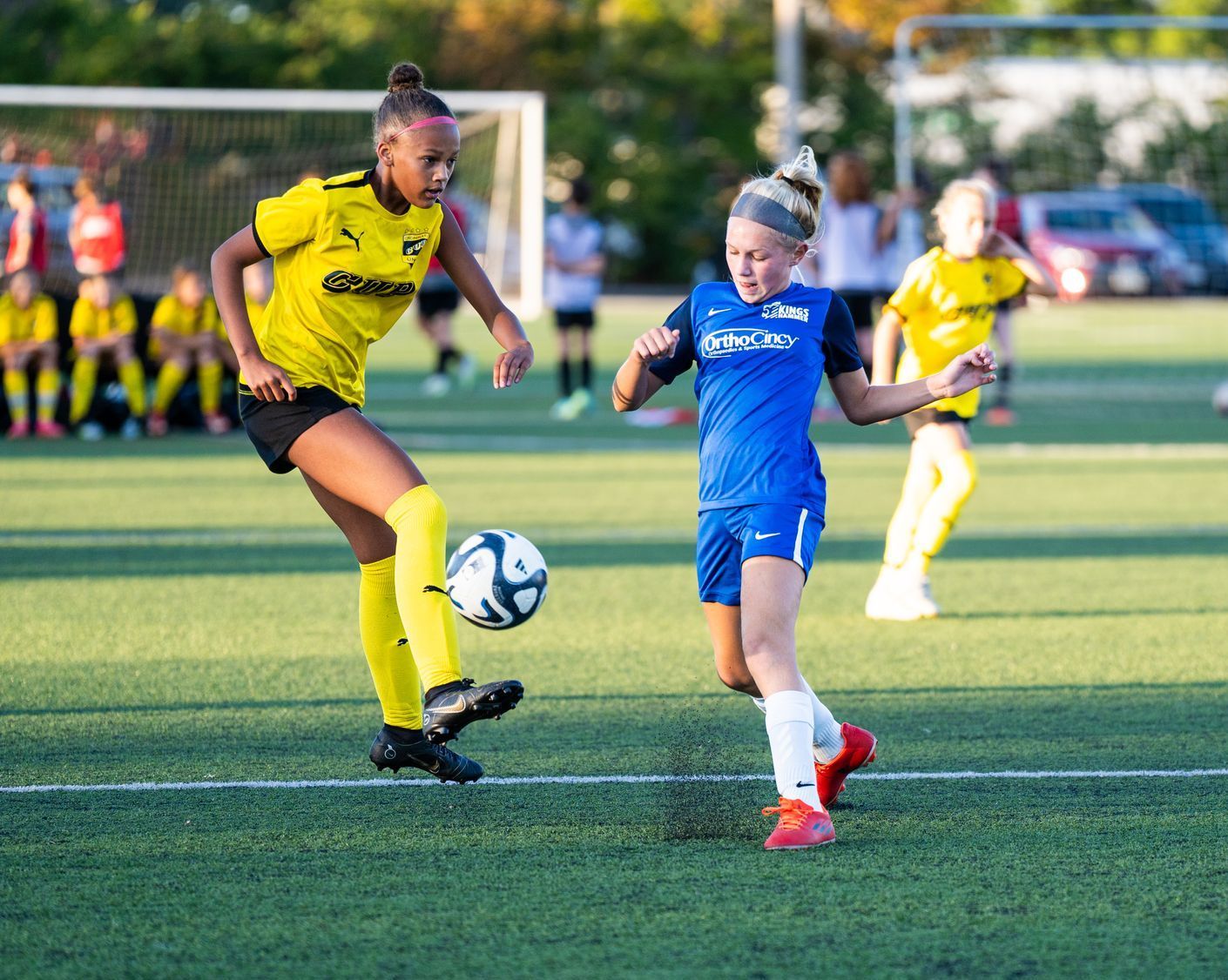 Two young girls are playing soccer on a field.