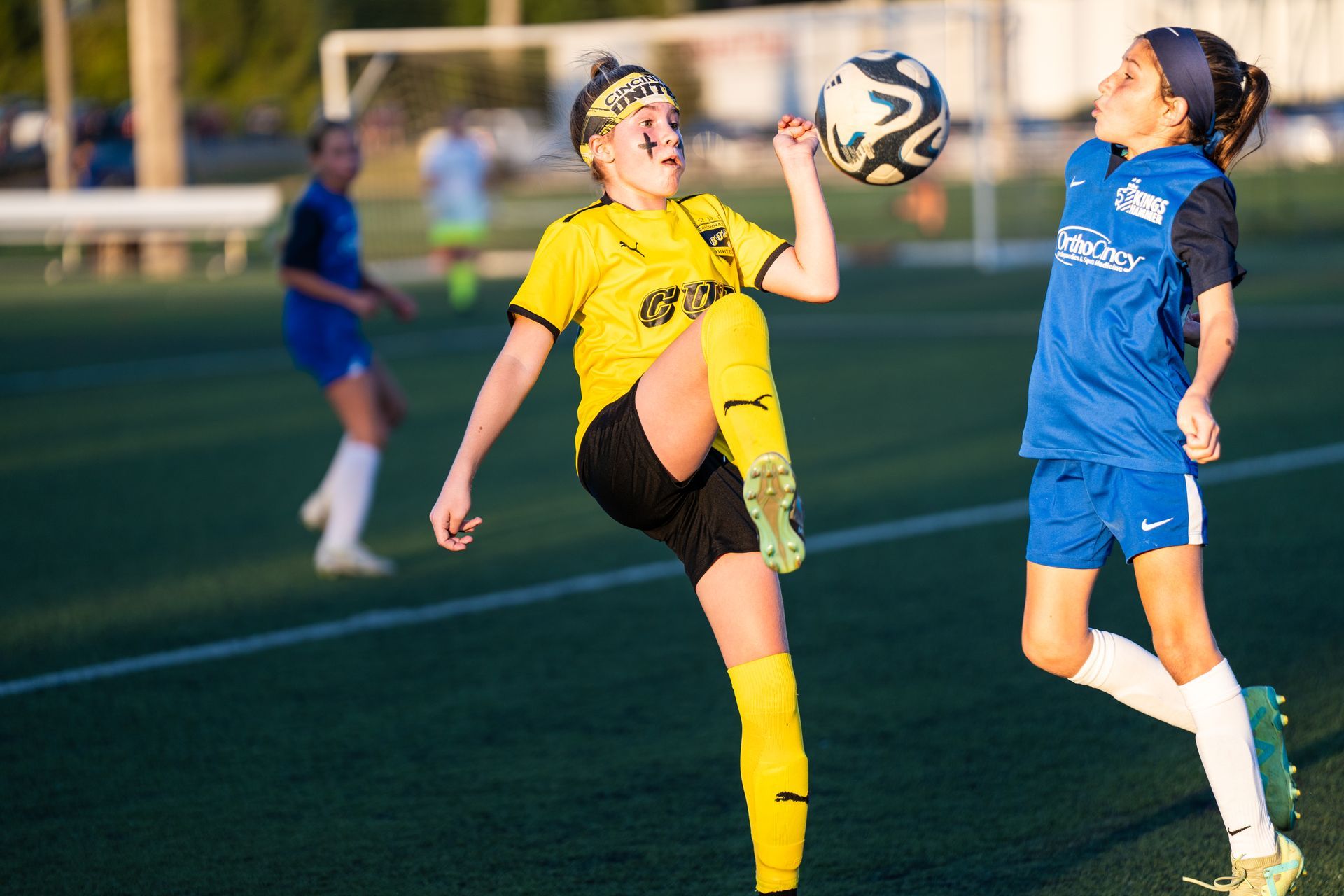 Two young girls are playing soccer on a field.
