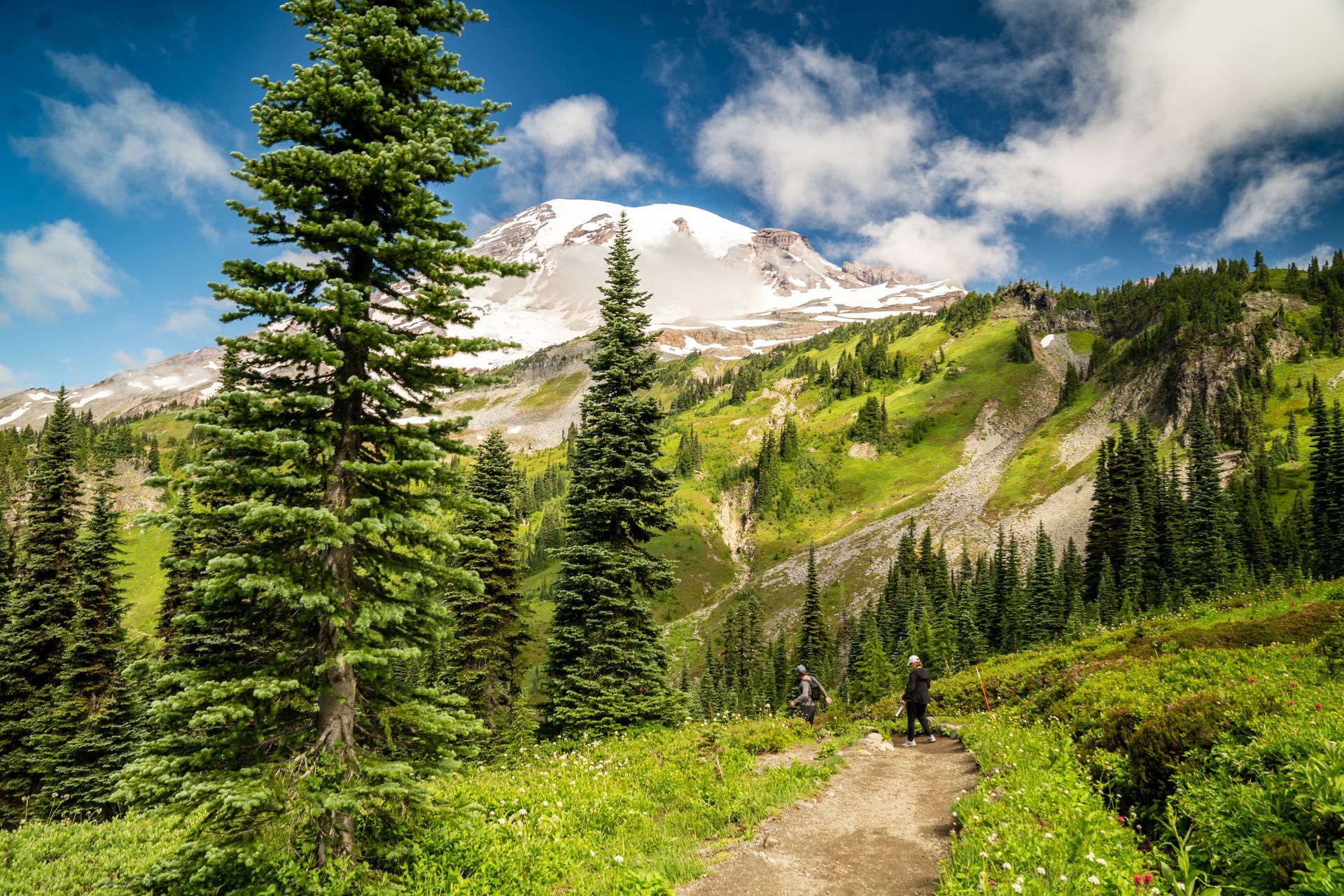 A person is walking down a trail in the mountains with a mountain in the background.