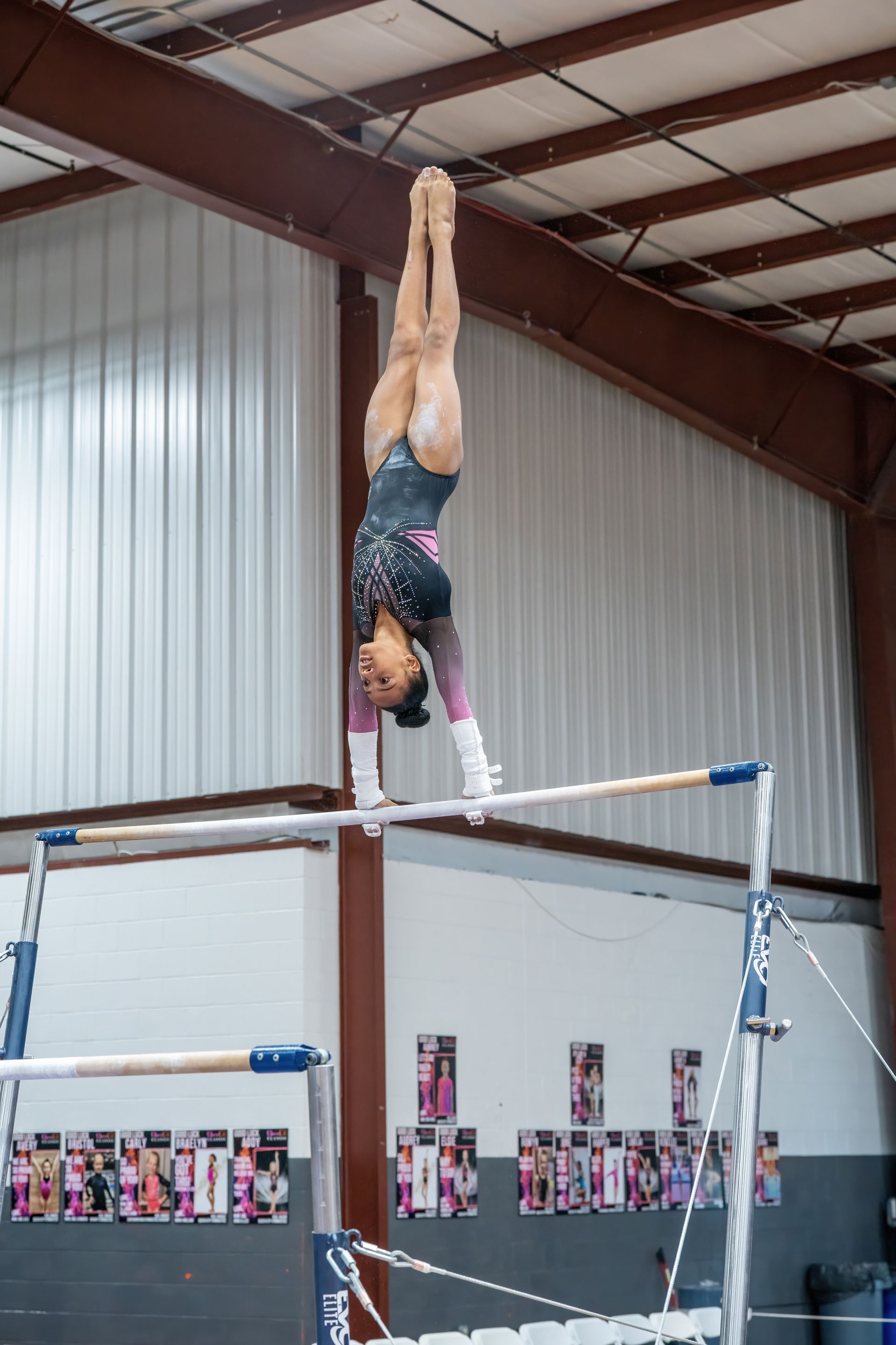 A female gymnast is doing a handstand on parallel bars in a gym.