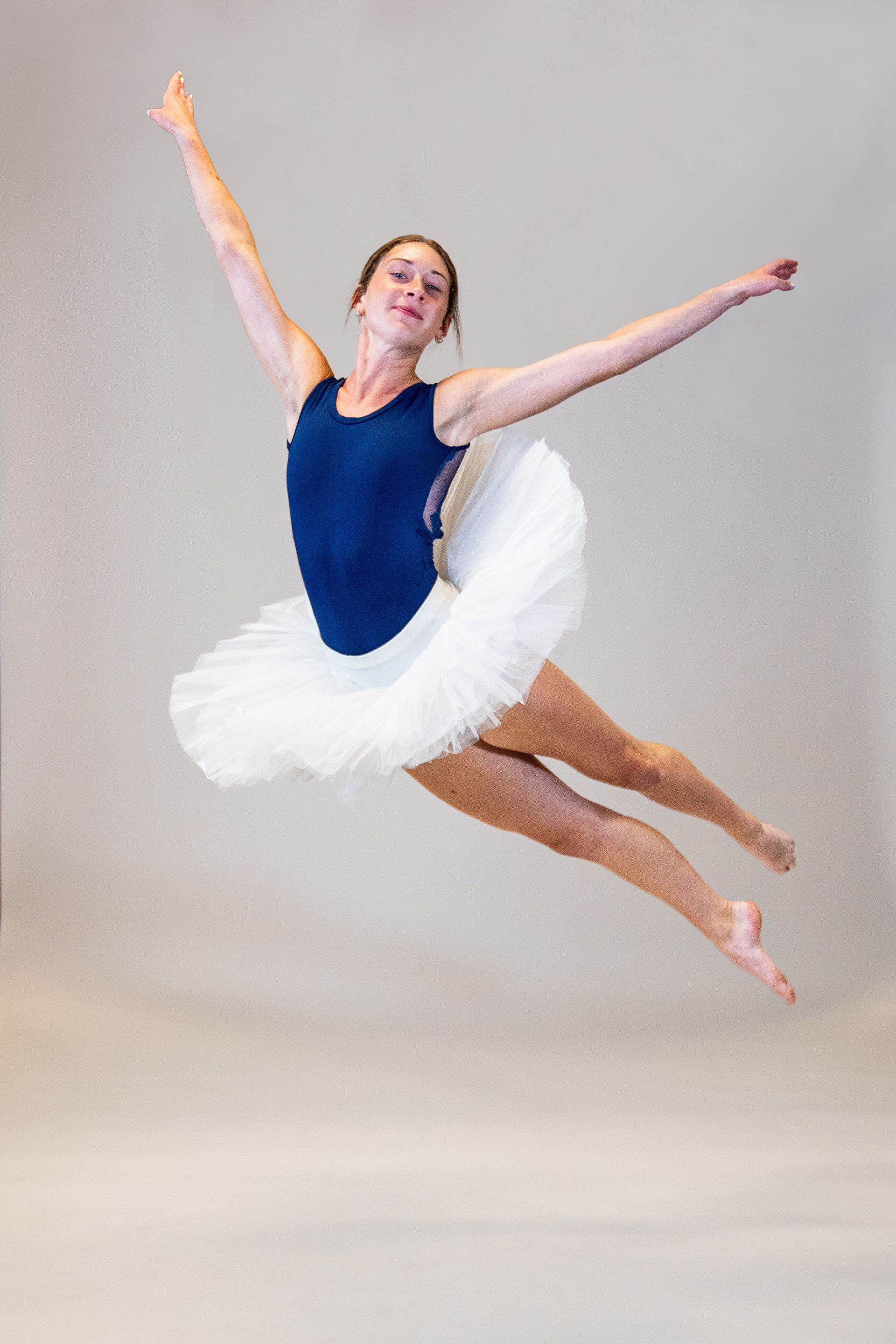 A ballerina in a blue leotard and white tutu is jumping in the air.