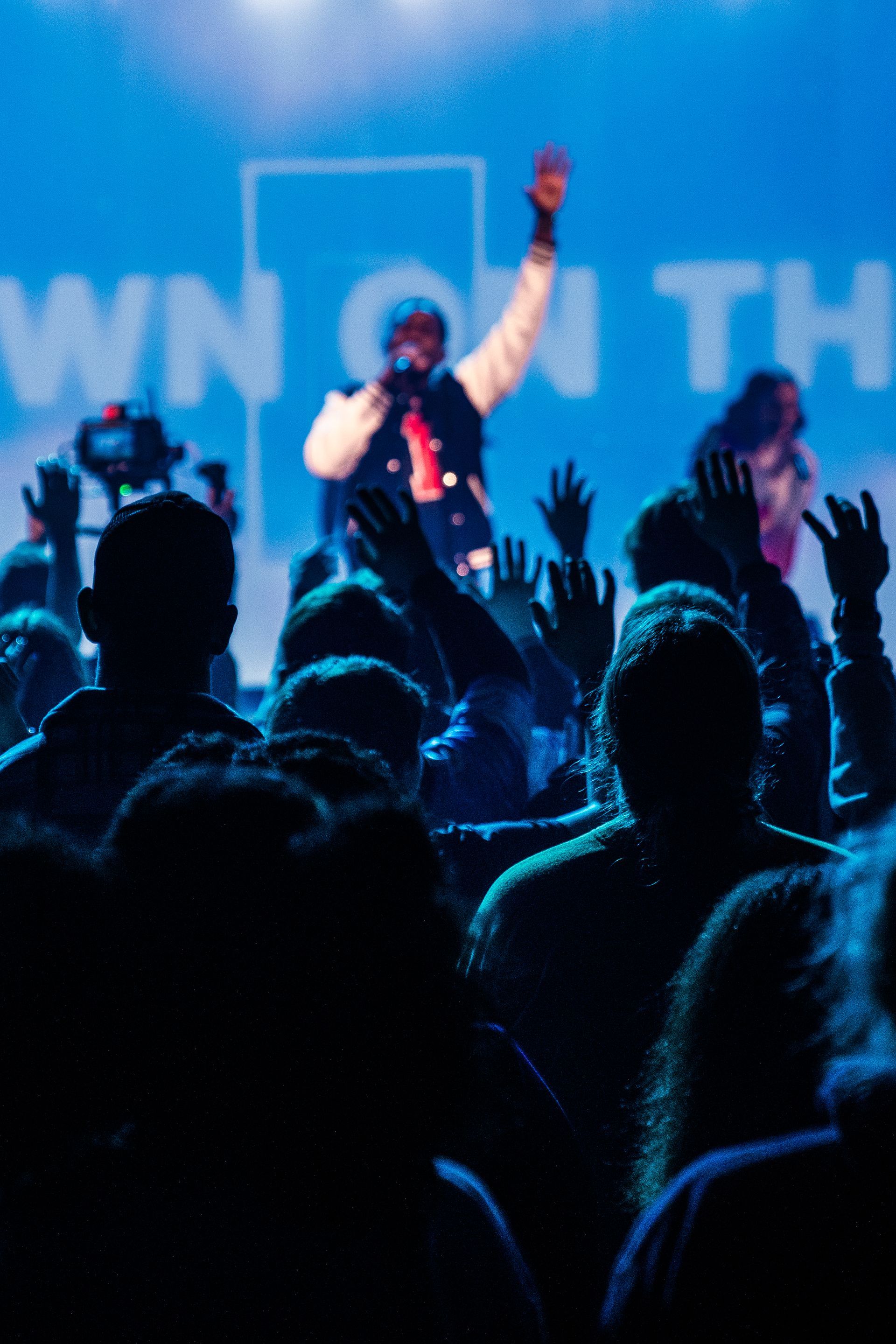 A man singing into a microphone in front of a crowd that is raising their hands in the air