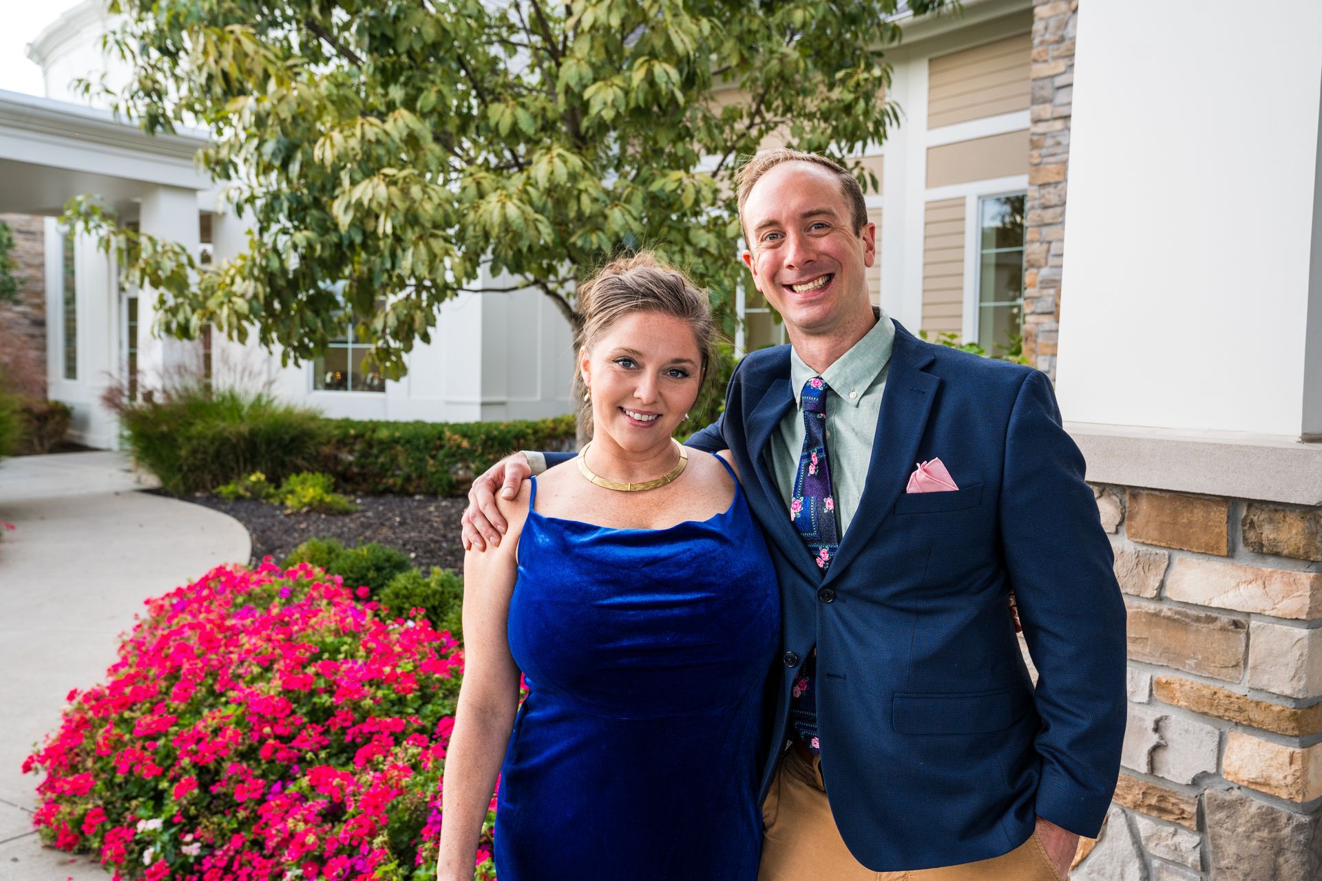 A man and a woman are posing for a picture in front of a house.