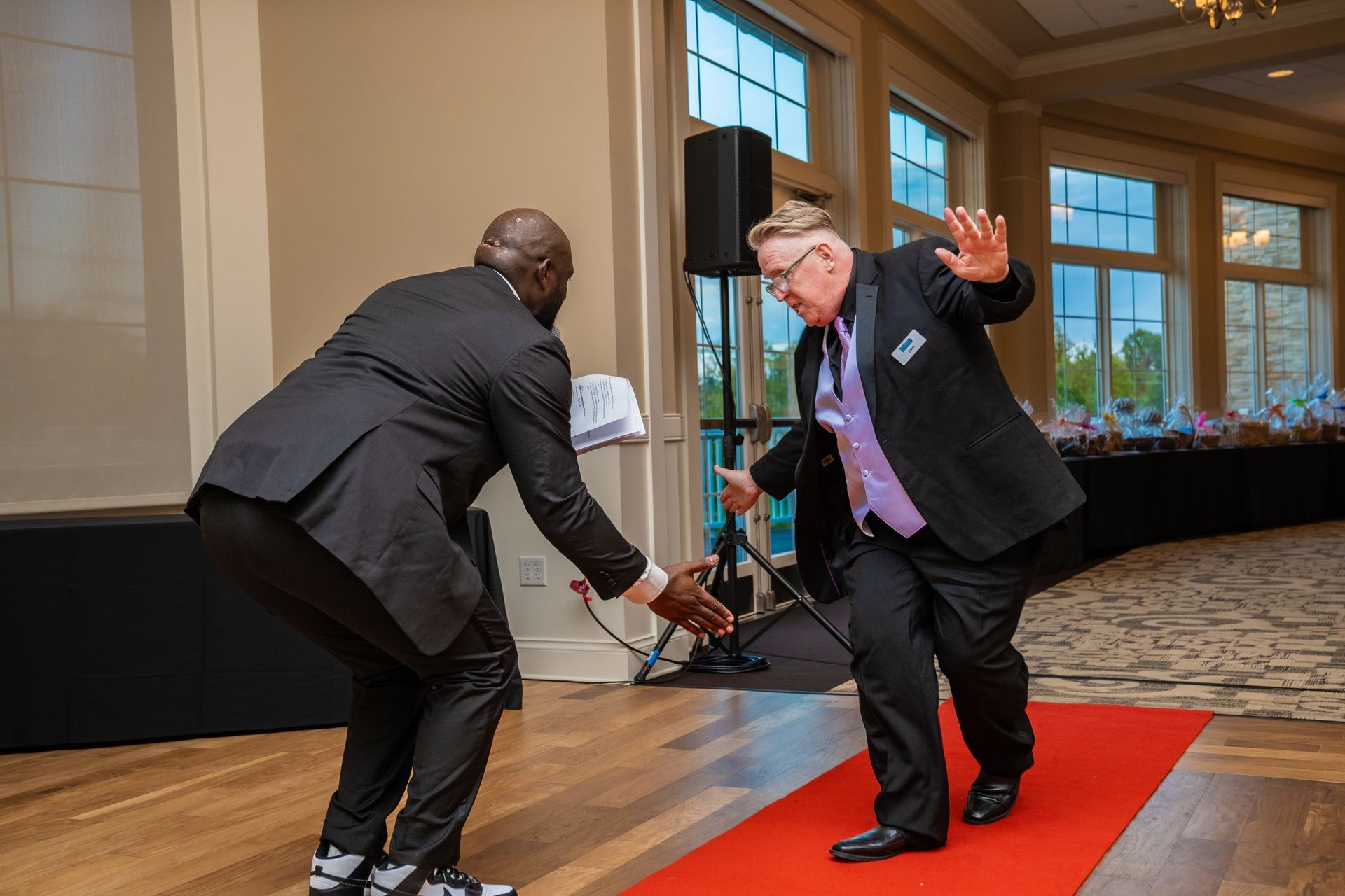 Two men in suits are dancing on a red carpet.
