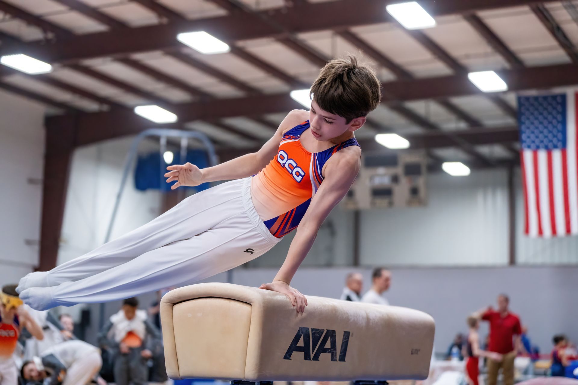 A young boy is doing a trick on a pommel horse in a gym.