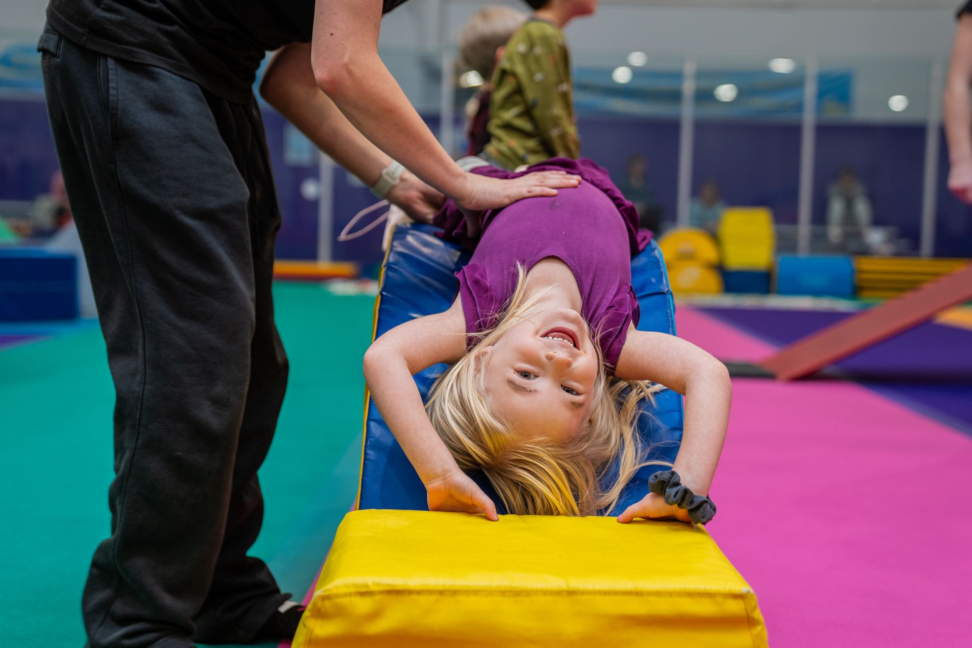A little girl is doing a handstand on a yellow block.