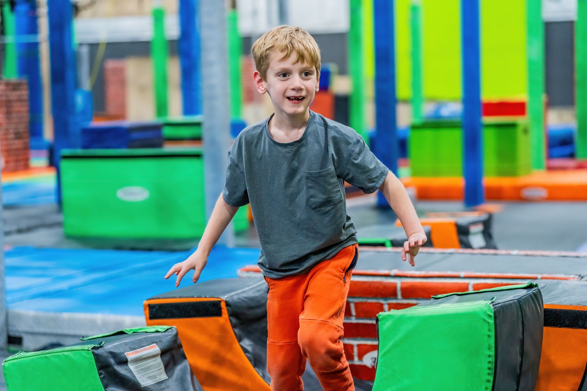 A young boy is jumping over a brick wall in a trampoline park.