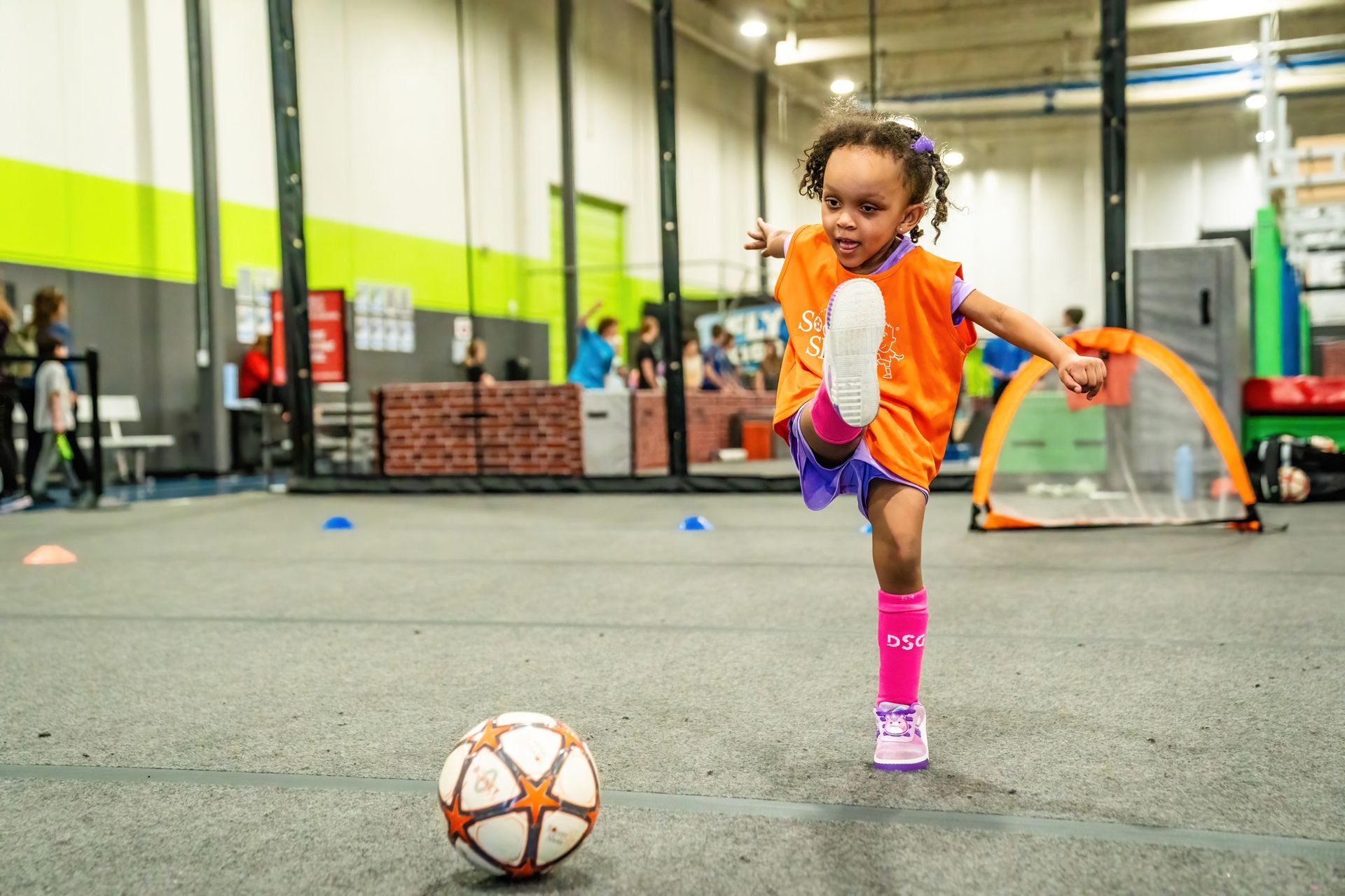 A little girl is kicking a soccer ball in a gym.