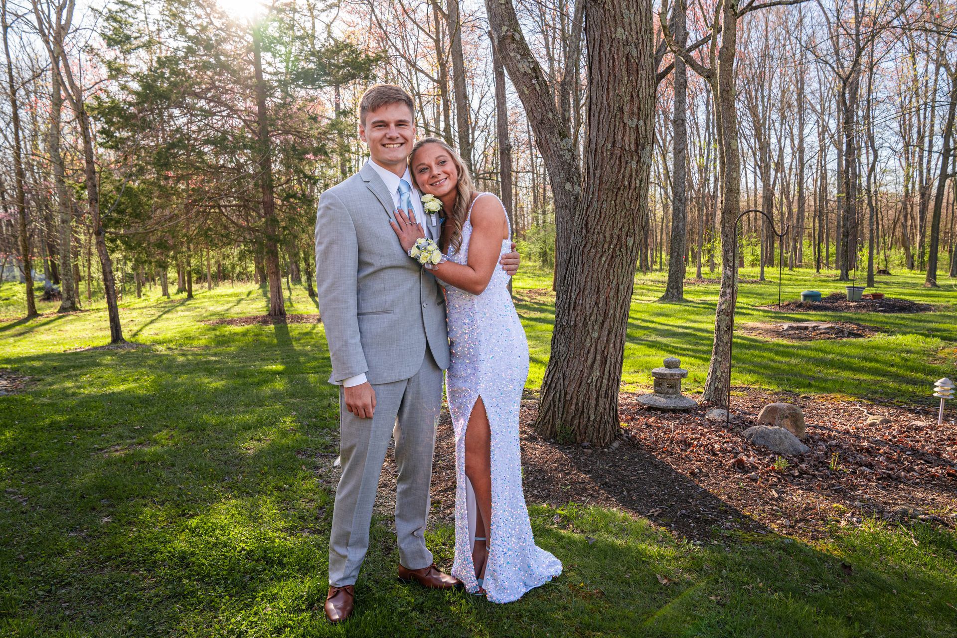 A teen boy and girl are posing for a picture in the woods.