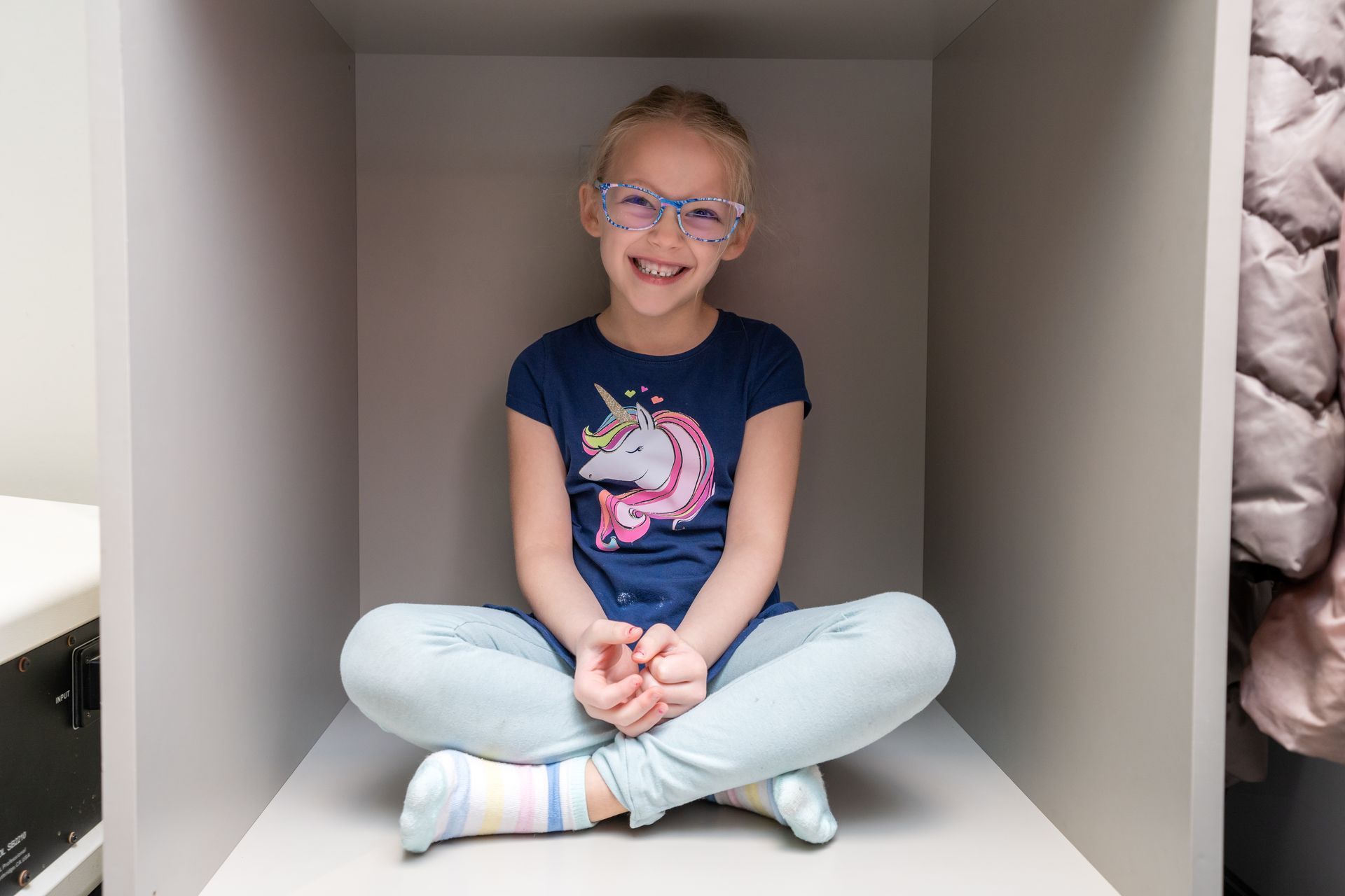 A little girl is sitting in a cube with her legs crossed.