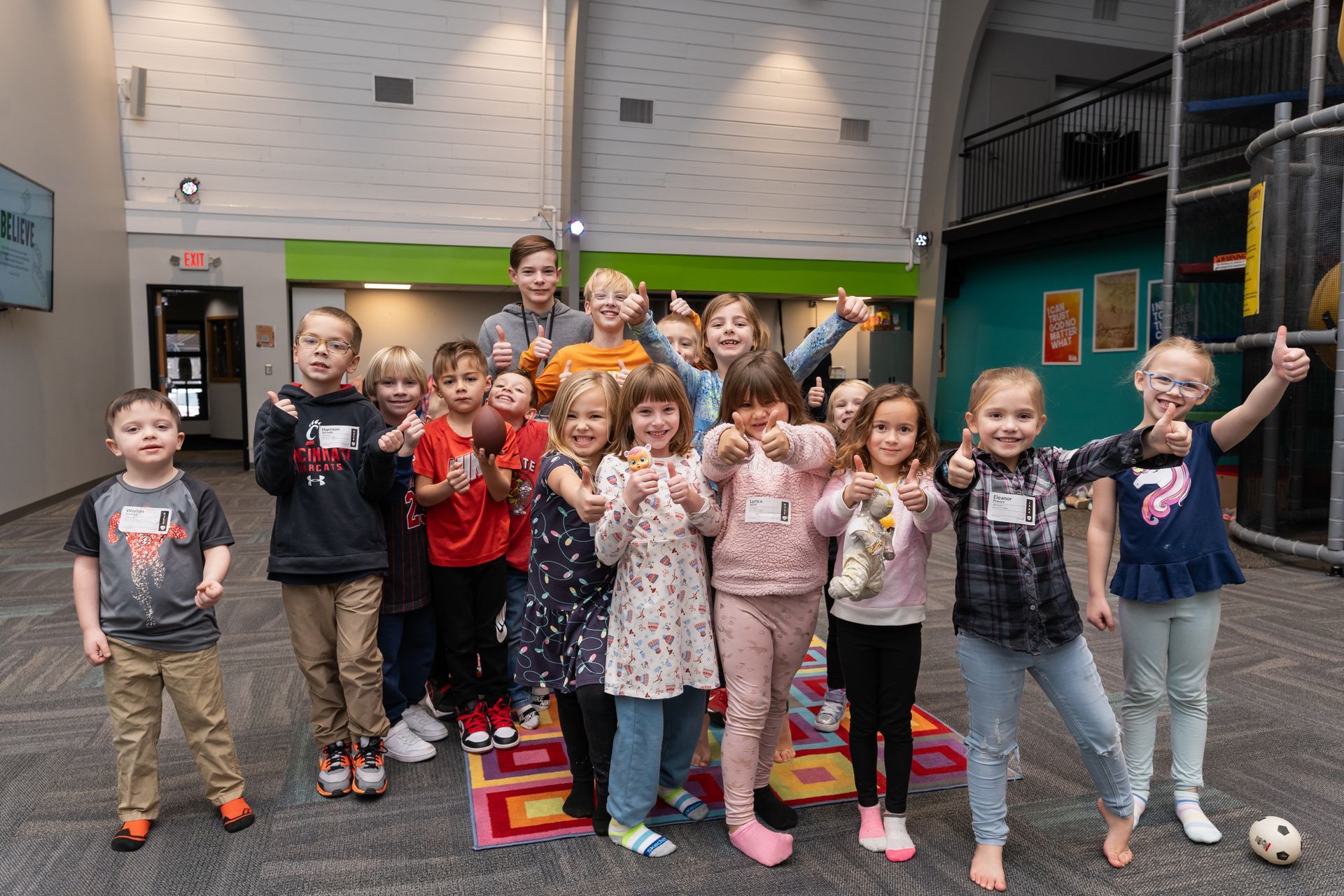 A group of children are posing for a picture and giving a thumbs up.