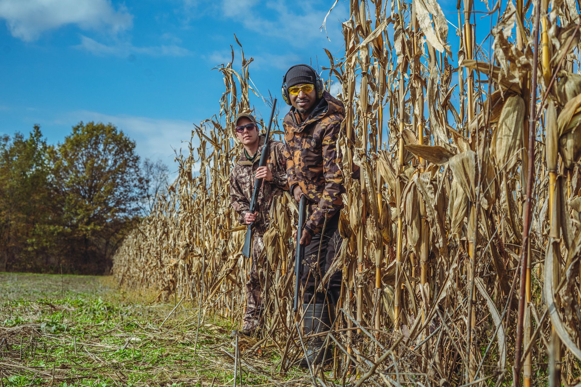 Two men in camouflage standing in a corn field.