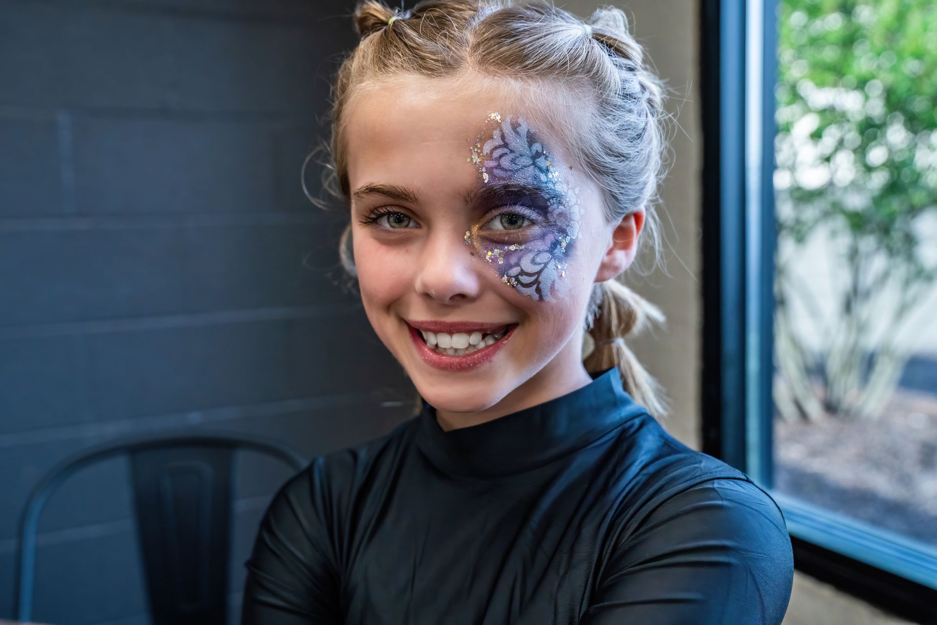 A young girl with face paint on her face is smiling for the camera.