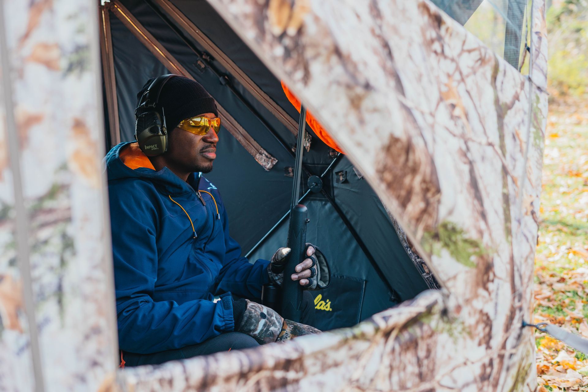 A man is sitting in a tent holding a bottle of beer.