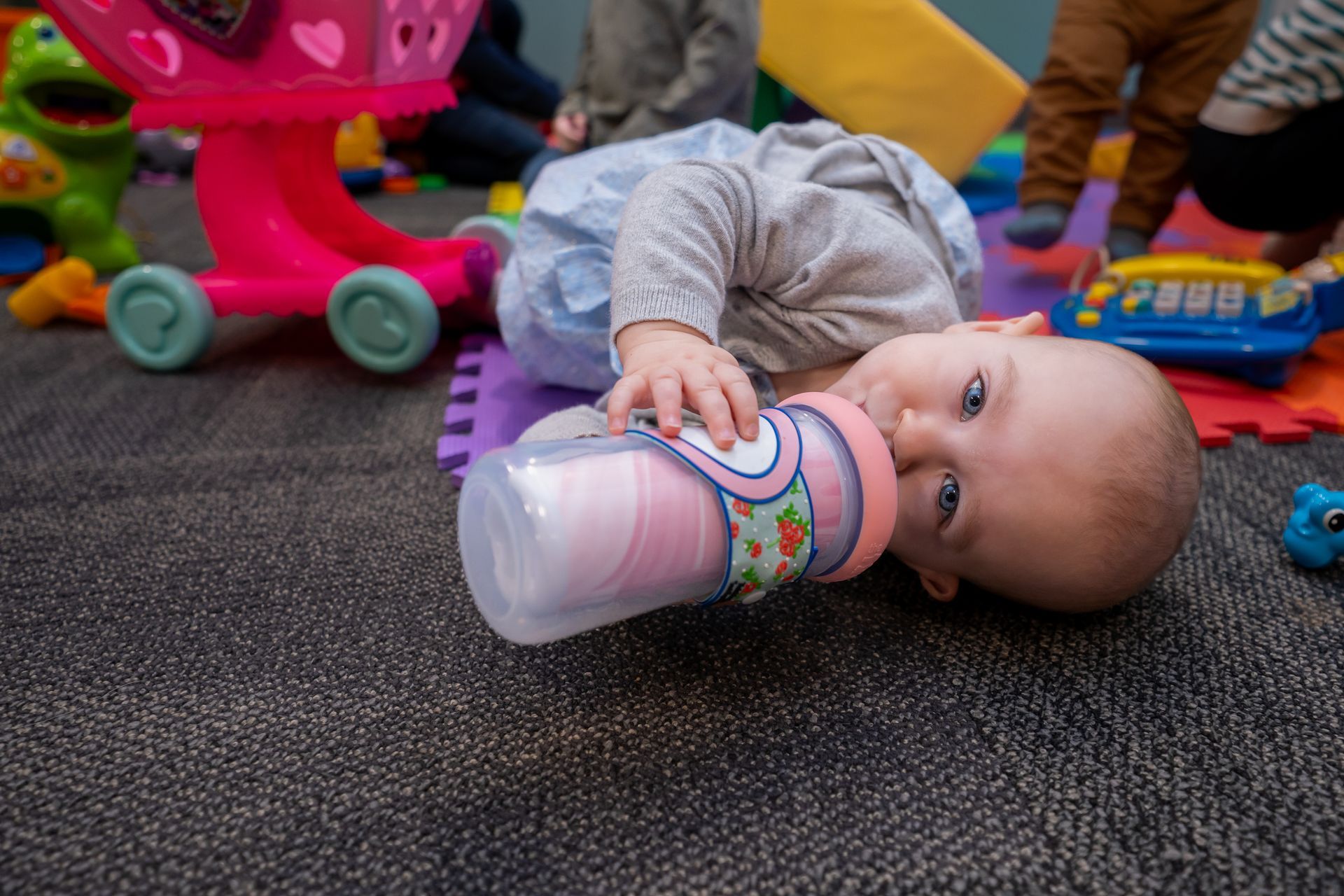 A baby is laying on the floor drinking from a bottle.