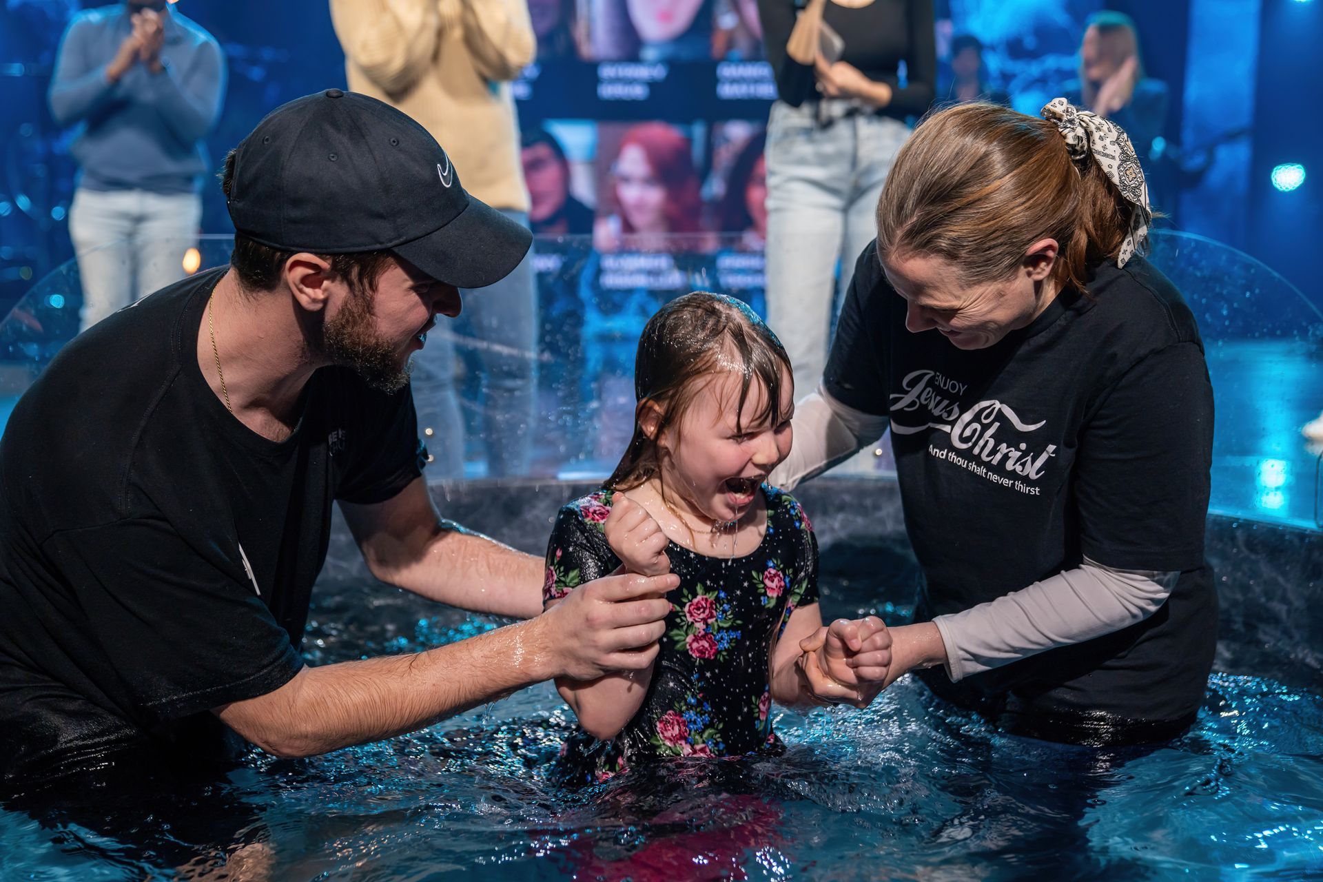 A man and woman are baptizing a little girl in a pool of water.