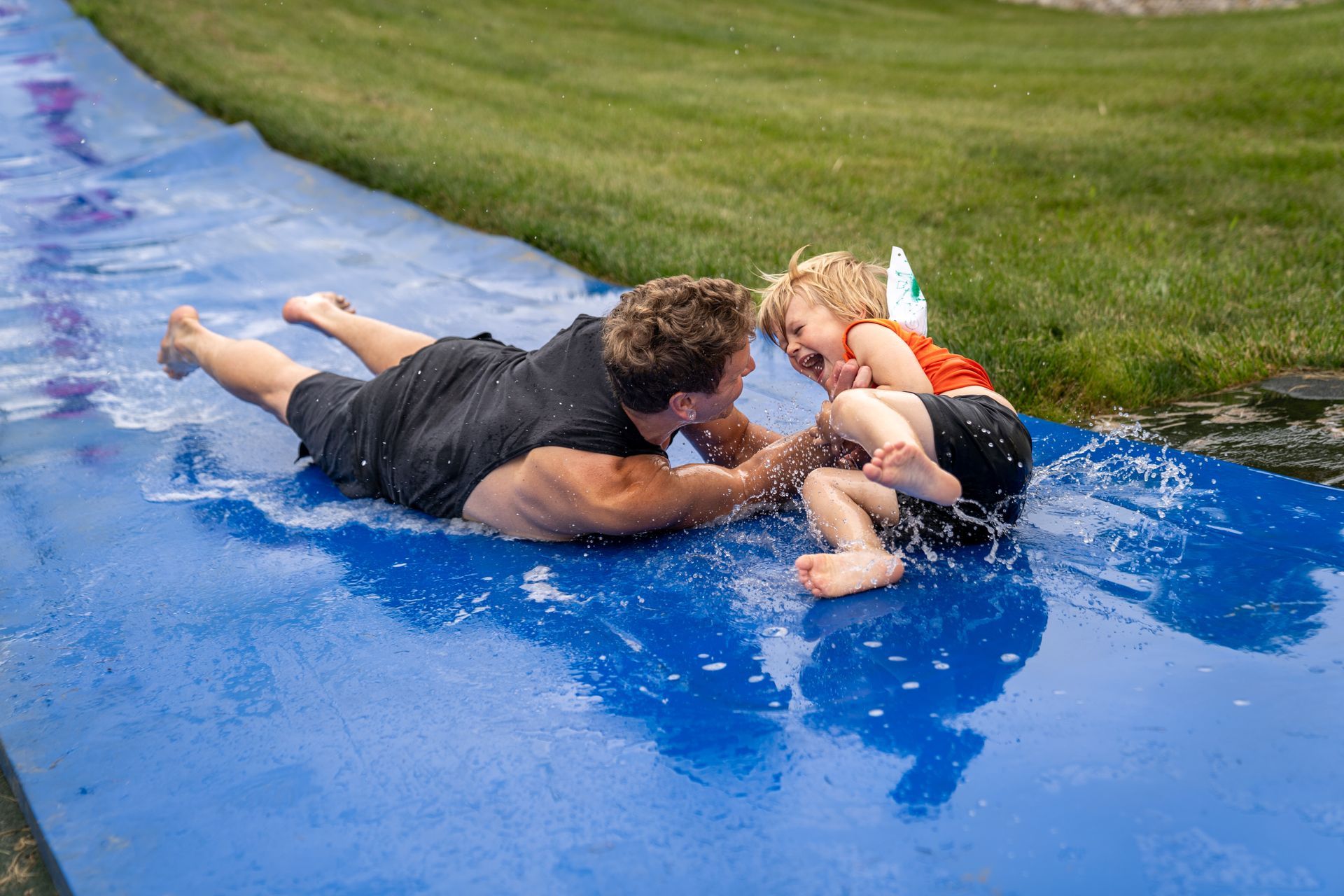 A man and two children are playing on a water slide.