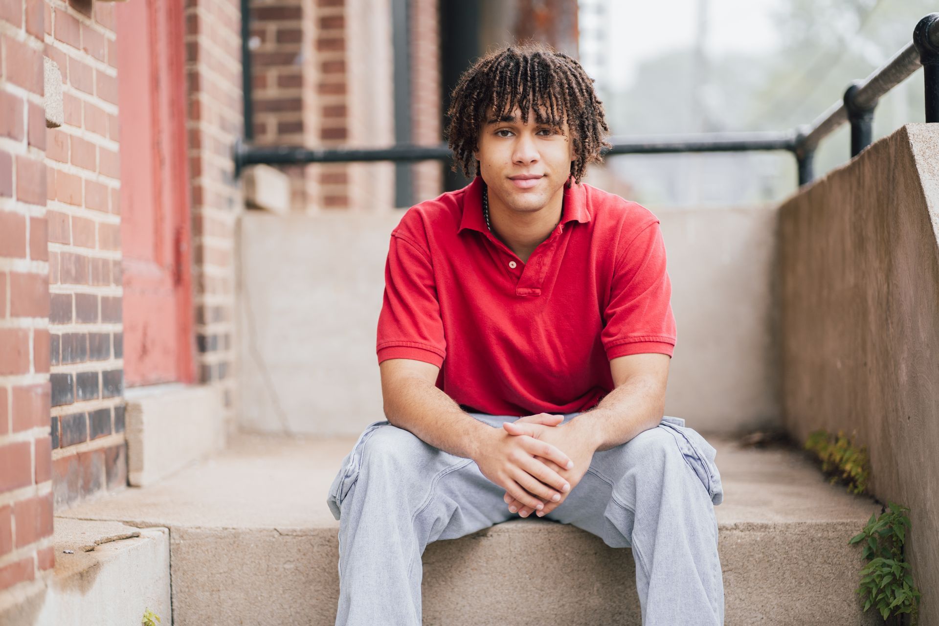 A young man in a red shirt is sitting on the steps of a building.