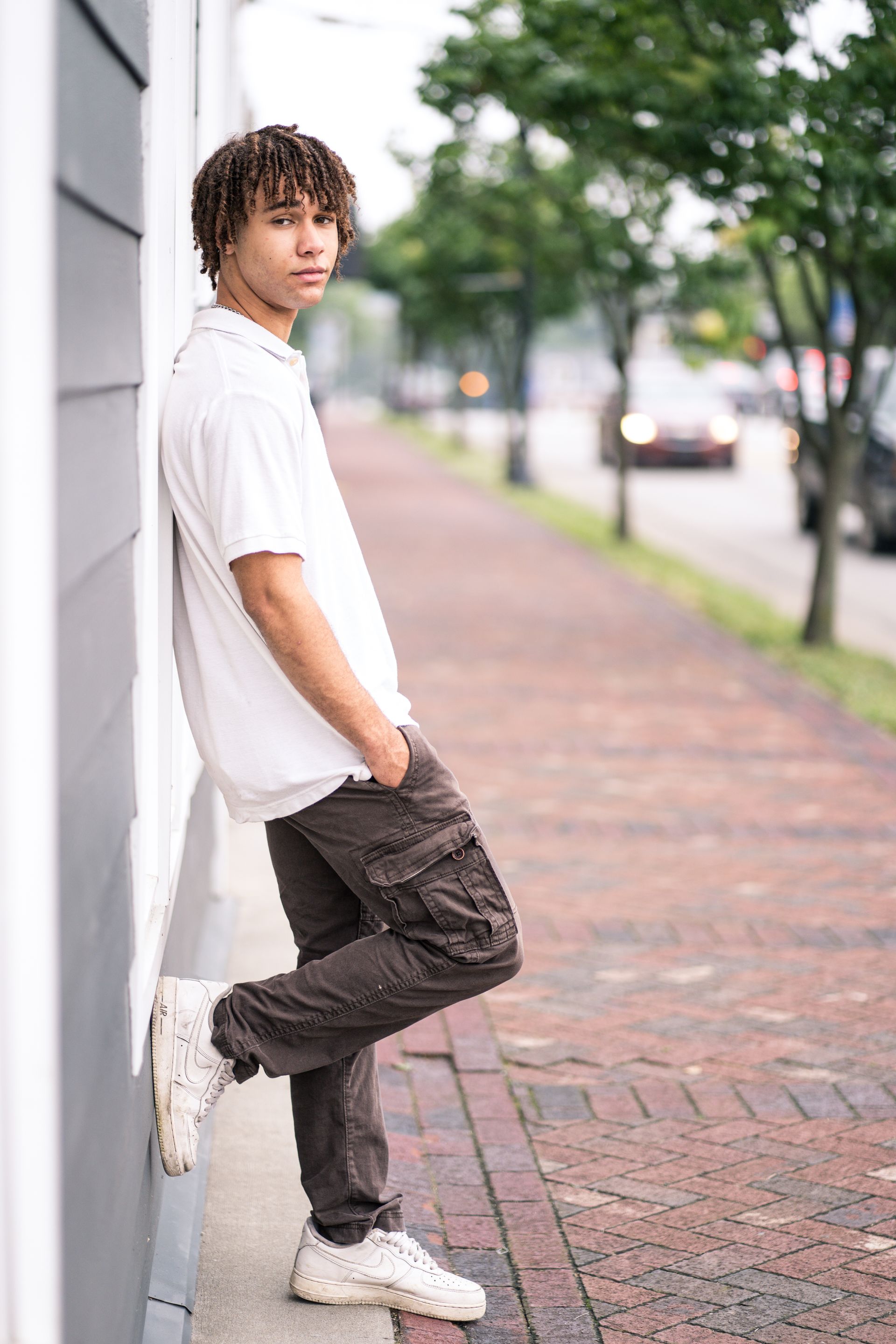 A young man leaning against a wall on a sidewalk.