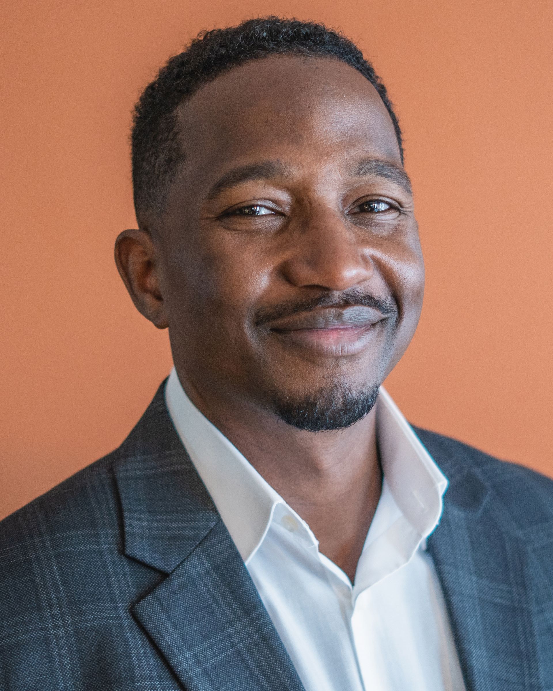 A man in a suit and white shirt is smiling for the camera.