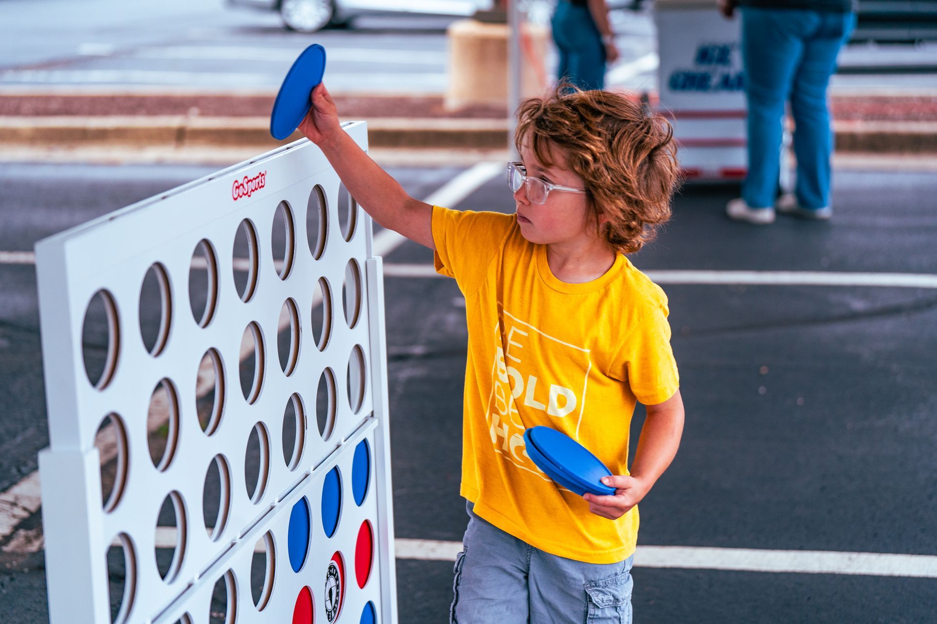 A young boy is playing a game of connect four in a parking lot.