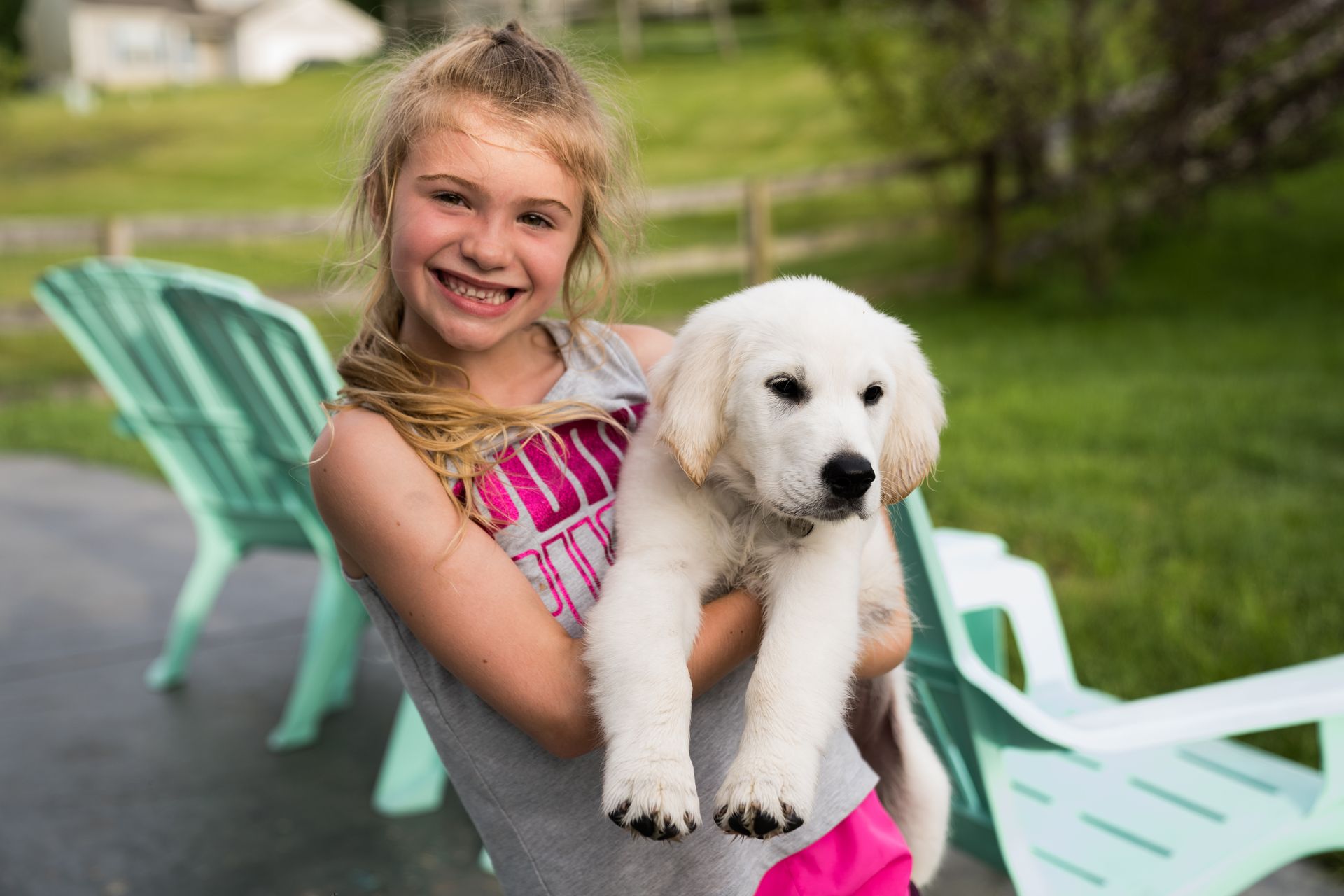 A little girl is holding a white puppy in her arms.