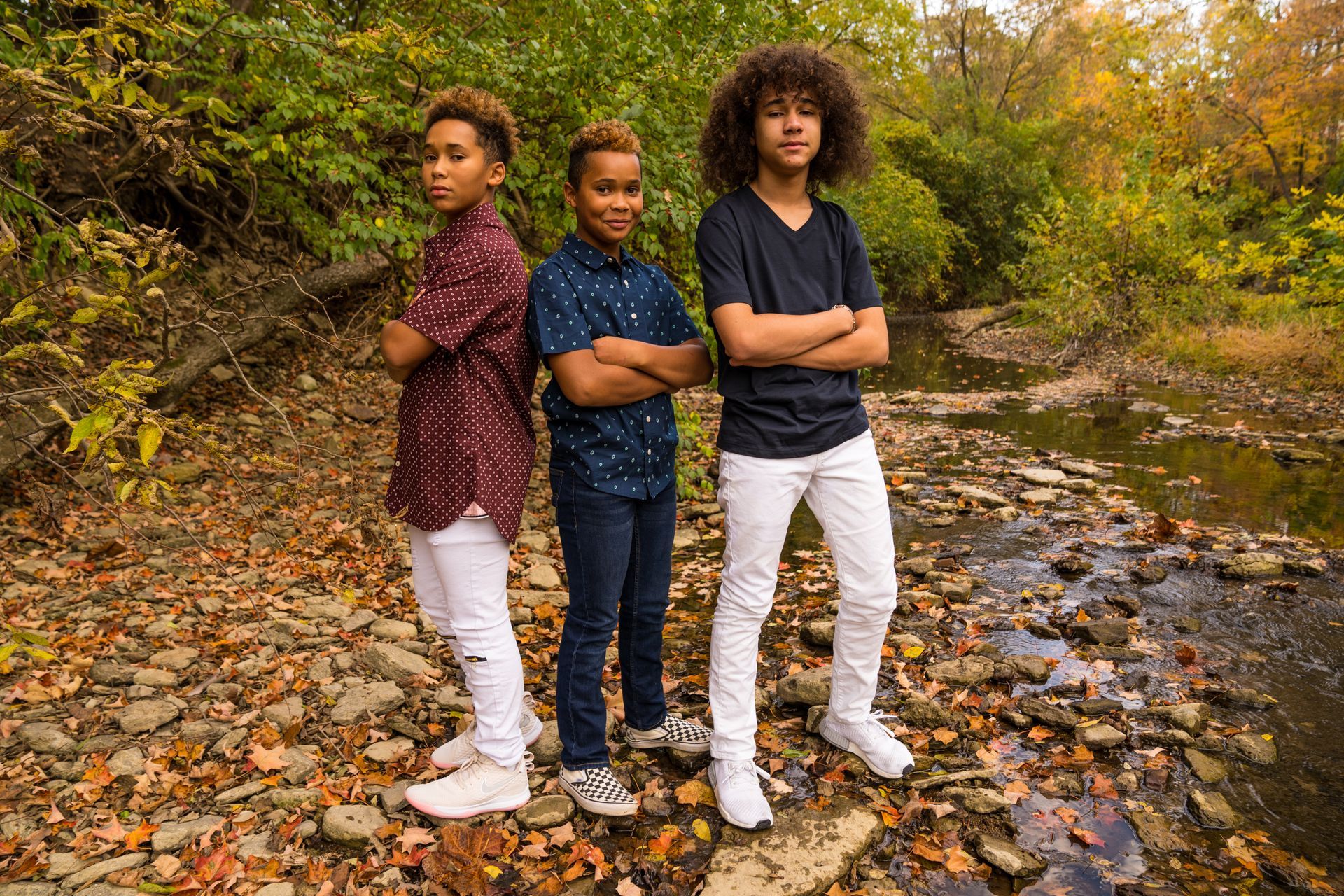 Three young boys are standing next to each other in front of a river.