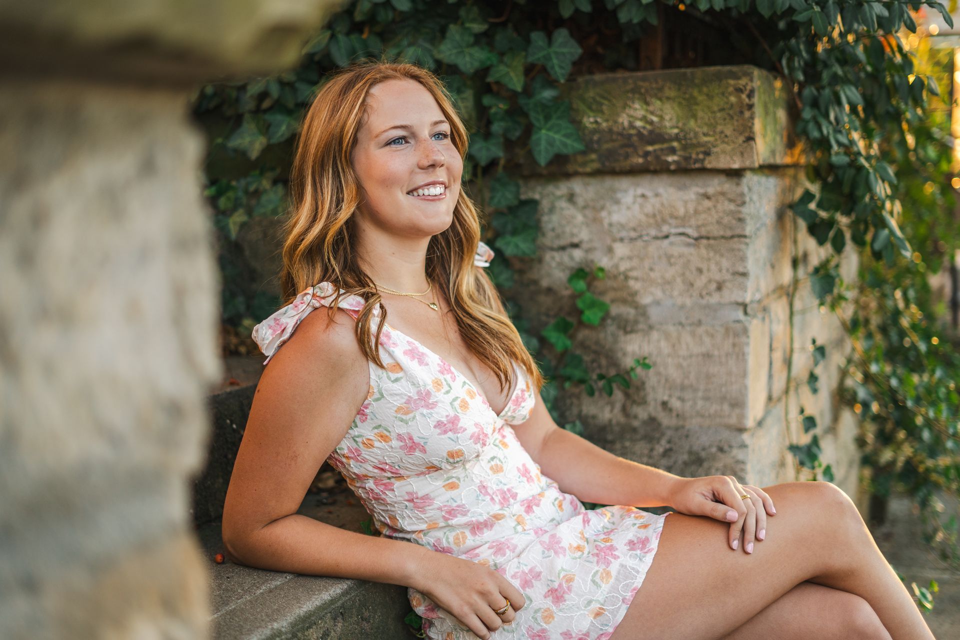 A woman in a floral dress is sitting on a stone wall.