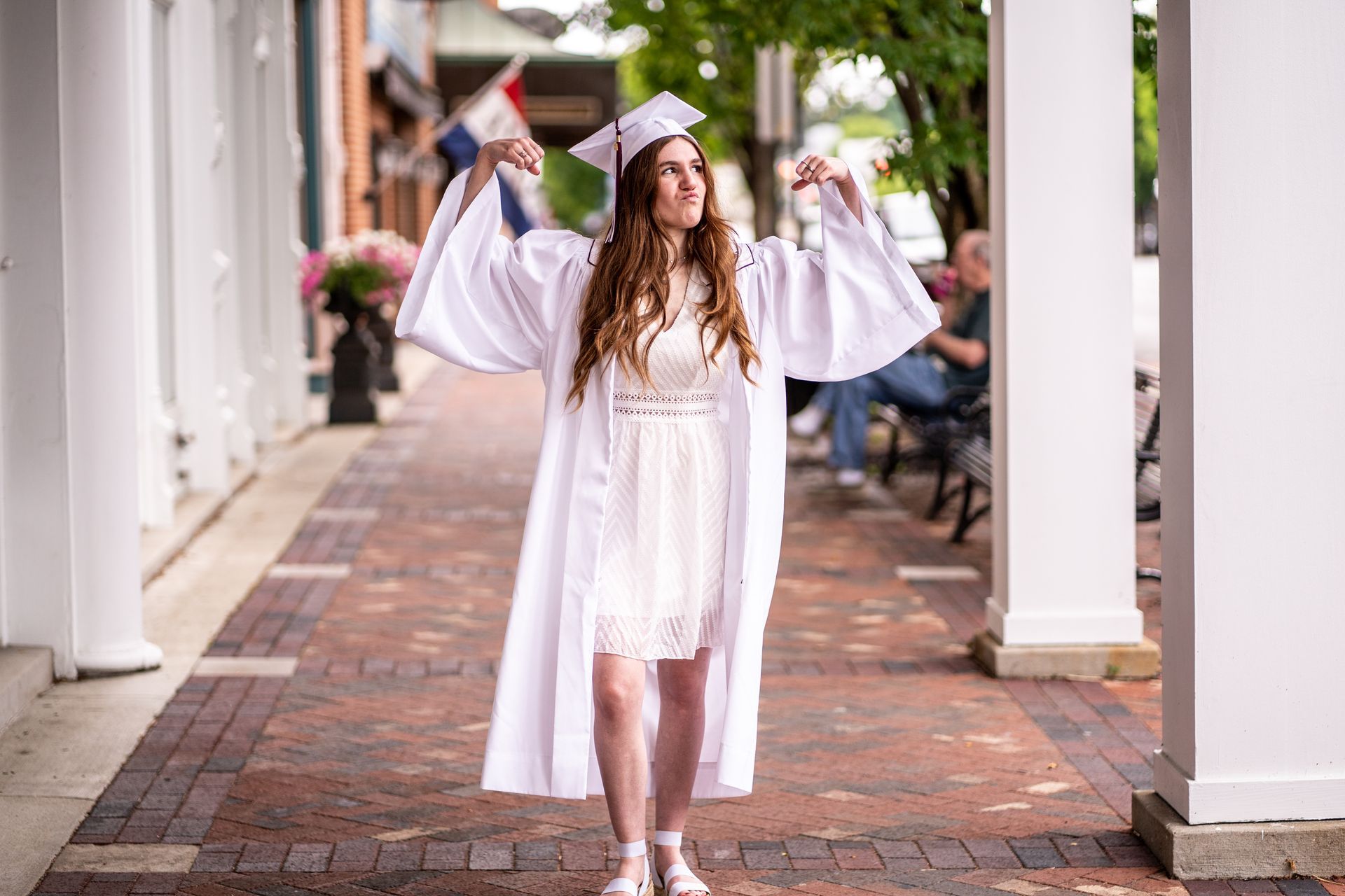 A woman in a graduation cap and gown is walking down a brick sidewalk.