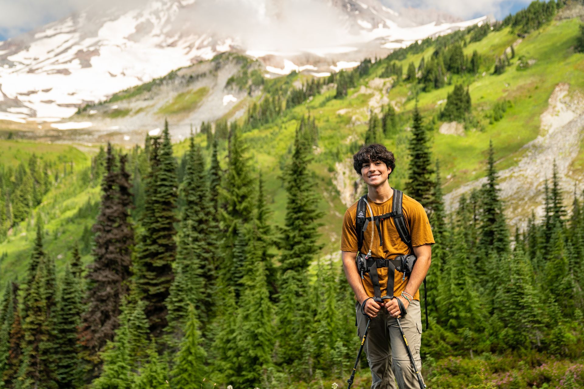A young man with a backpack is standing in front of a mountain.