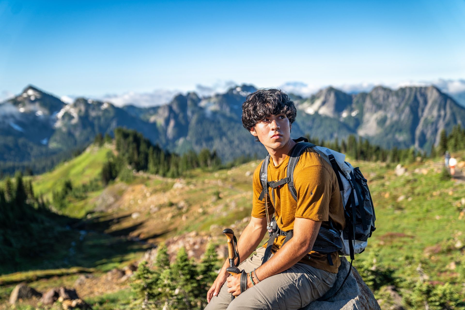 A young man with a backpack is sitting on a rock in the mountains.