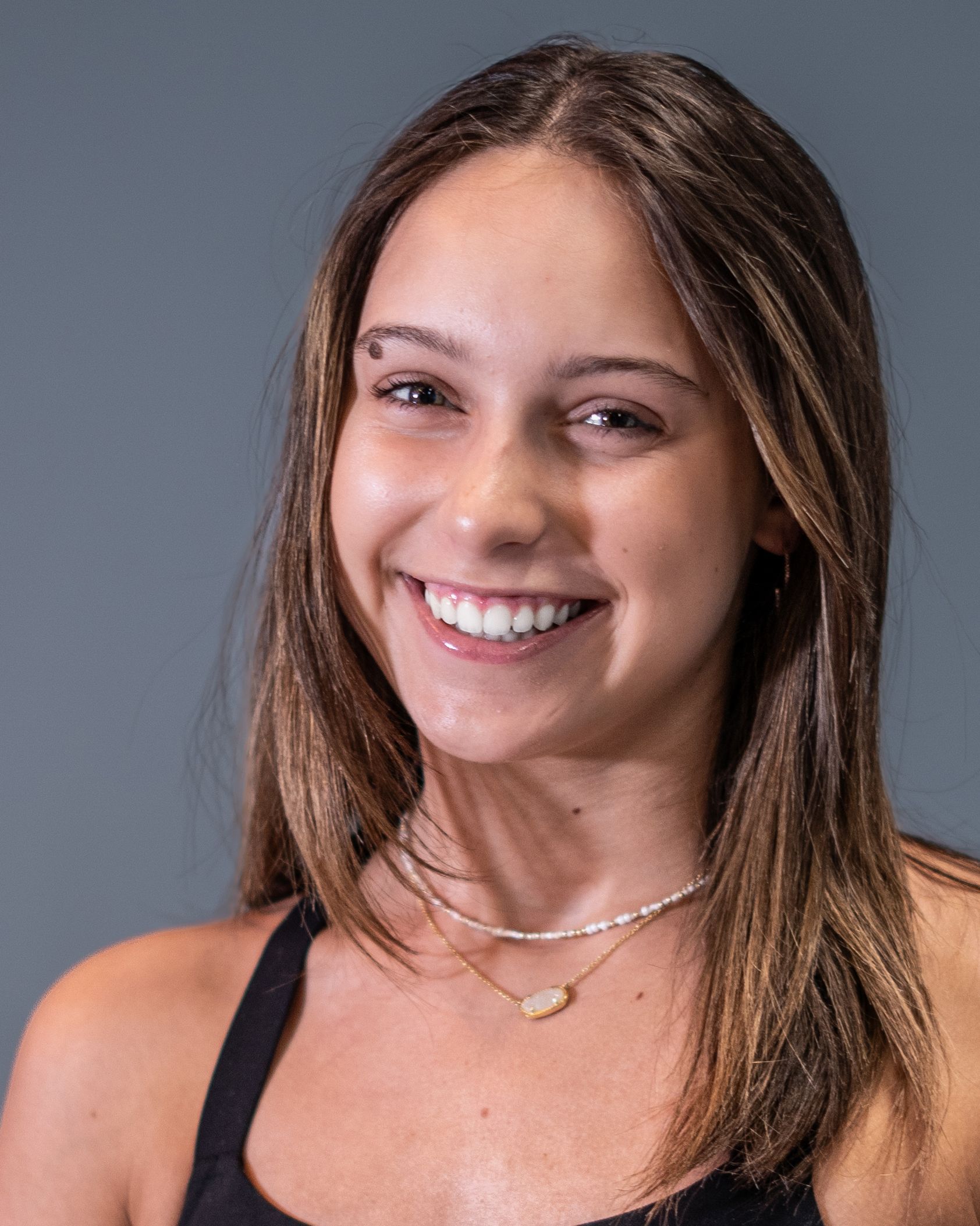 A young woman wearing a black tank top and a necklace is smiling for the camera.