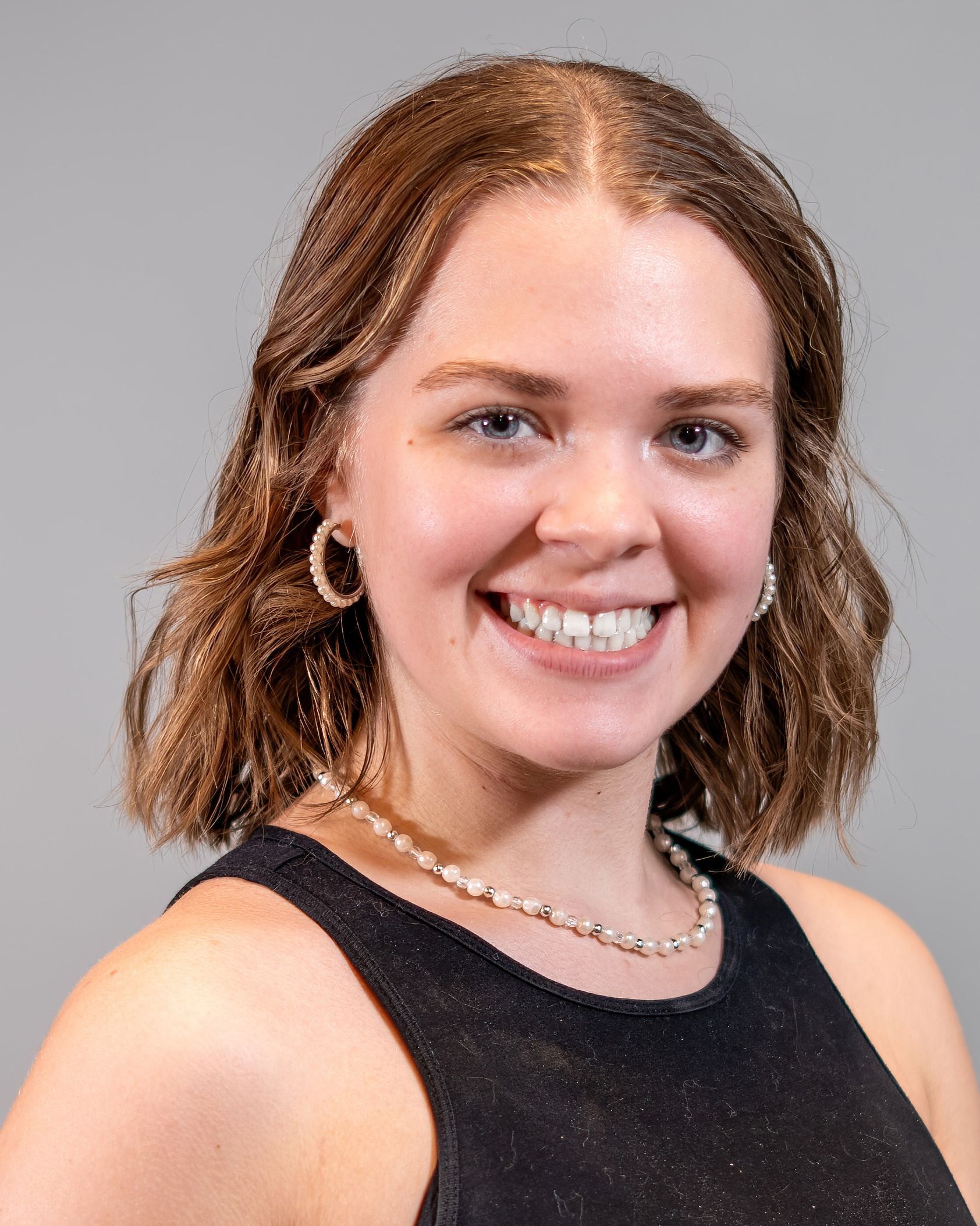A woman wearing a black tank top and a necklace is smiling for the camera.