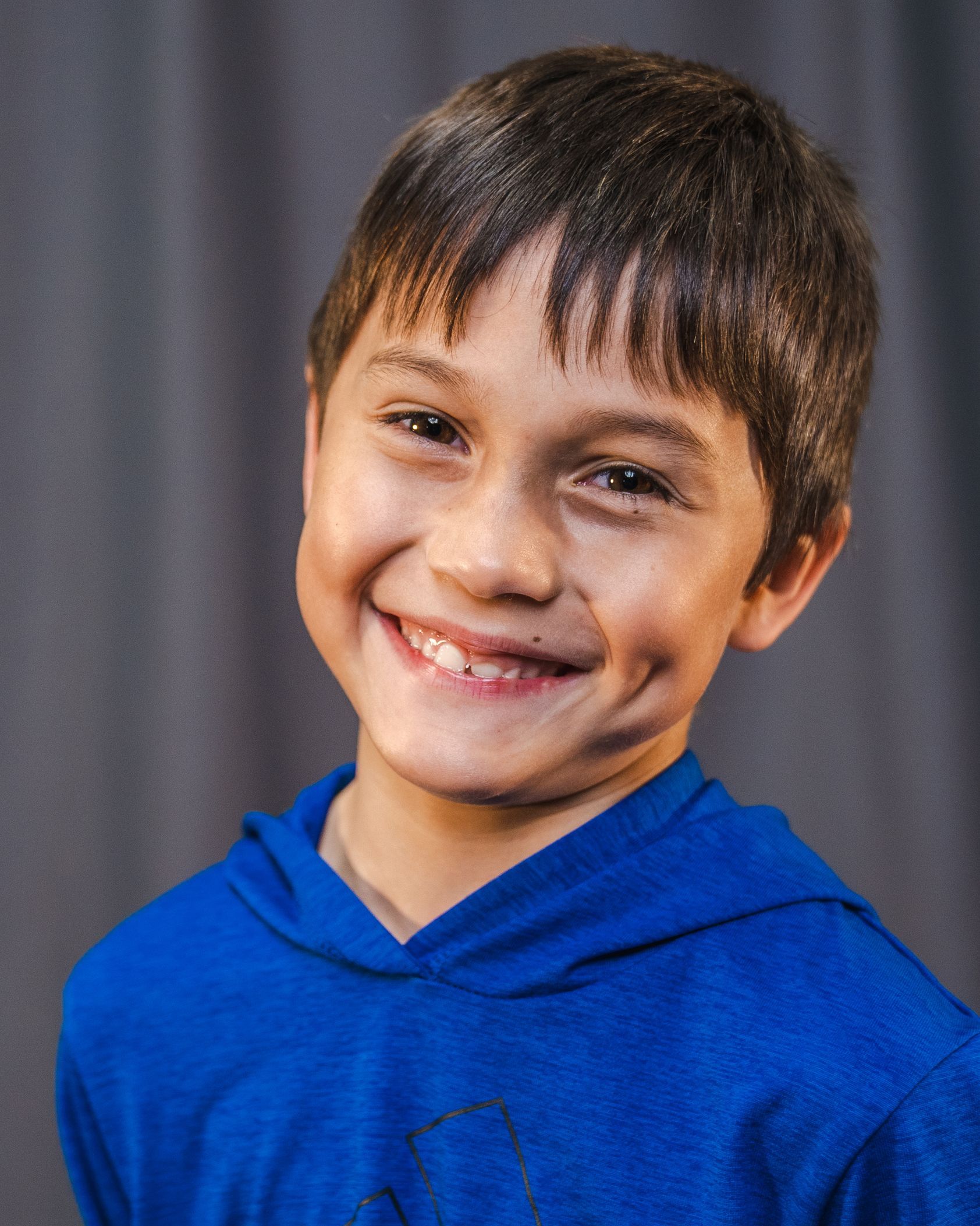 A young boy wearing a blue hoodie is smiling for the camera.