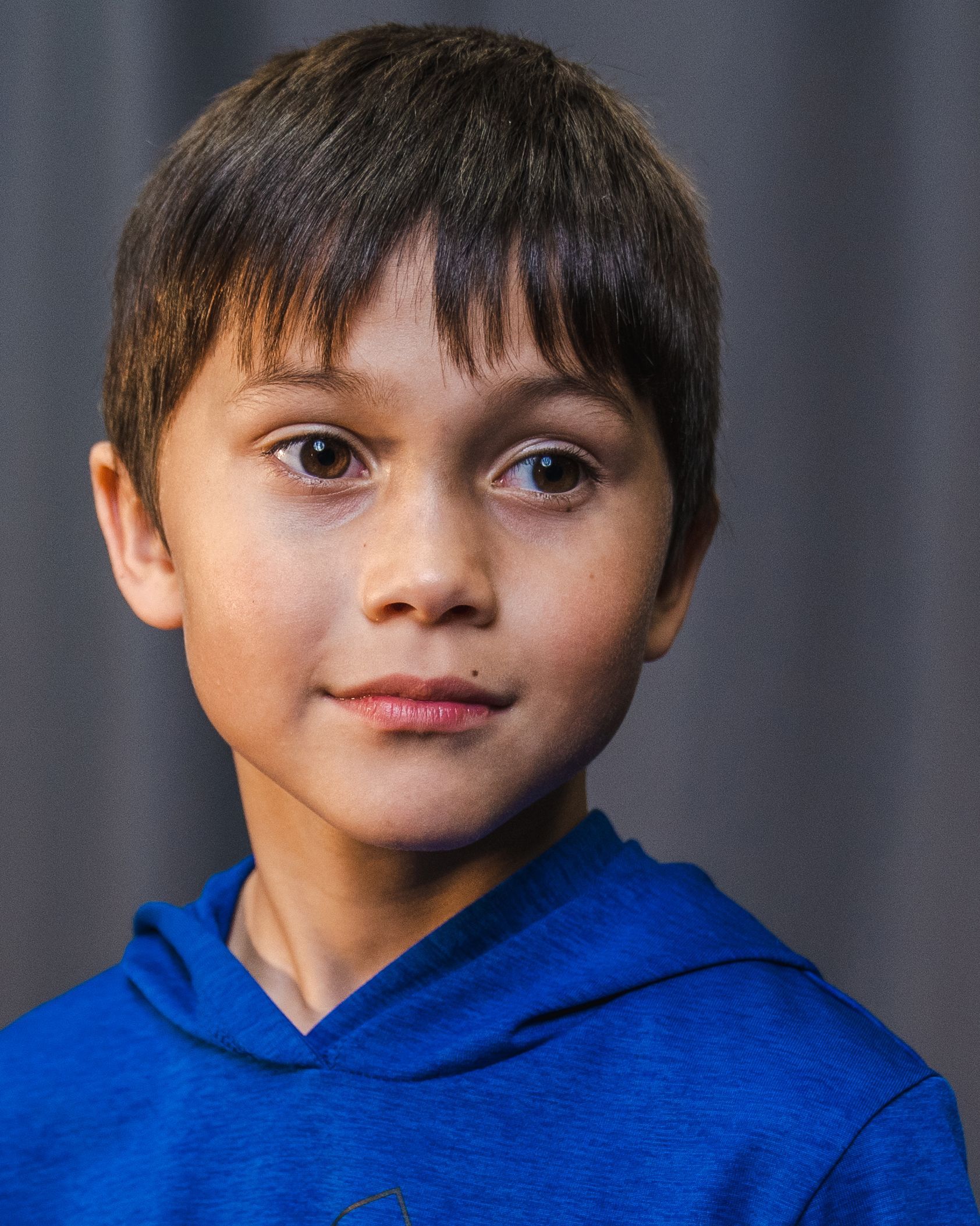 A young boy wearing a blue hoodie is looking at the camera.
