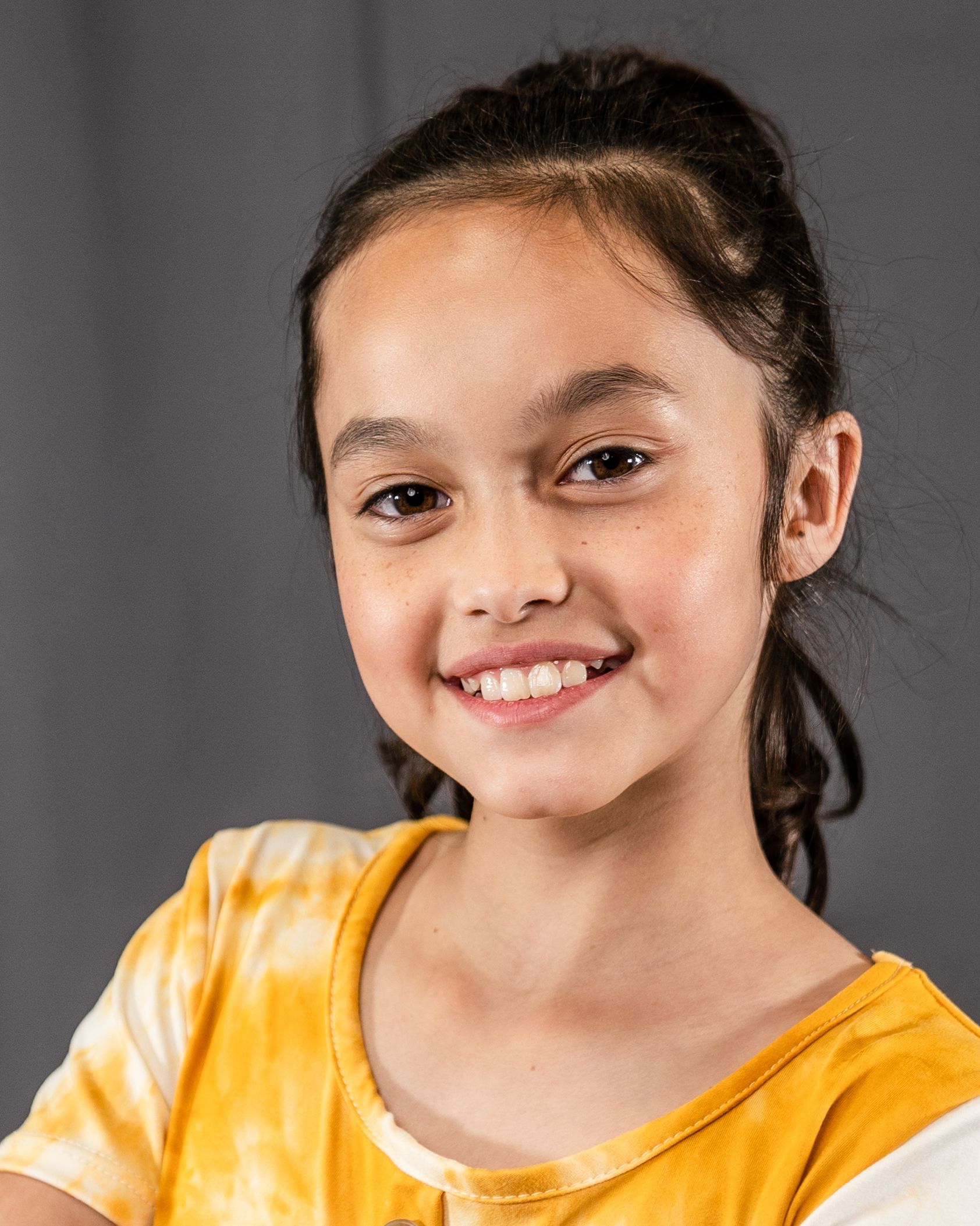 A young girl in a yellow shirt is smiling for the camera.