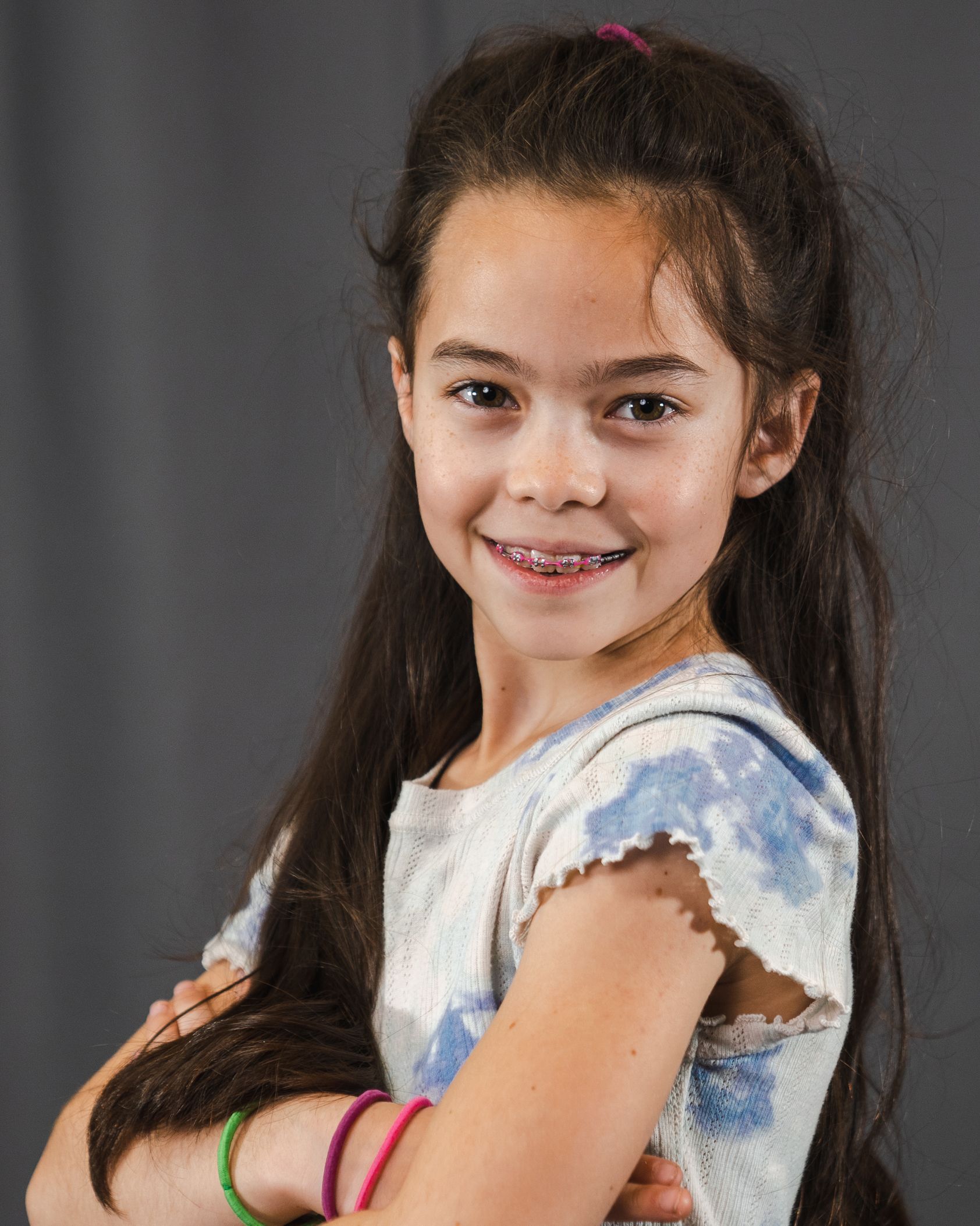A little girl with braces on her teeth is smiling for the camera.
